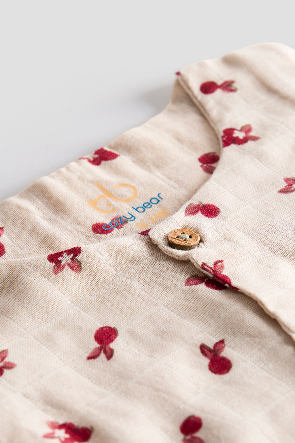 Close-up of a baby garment with floral patterns and a visible brand logo on a light background.