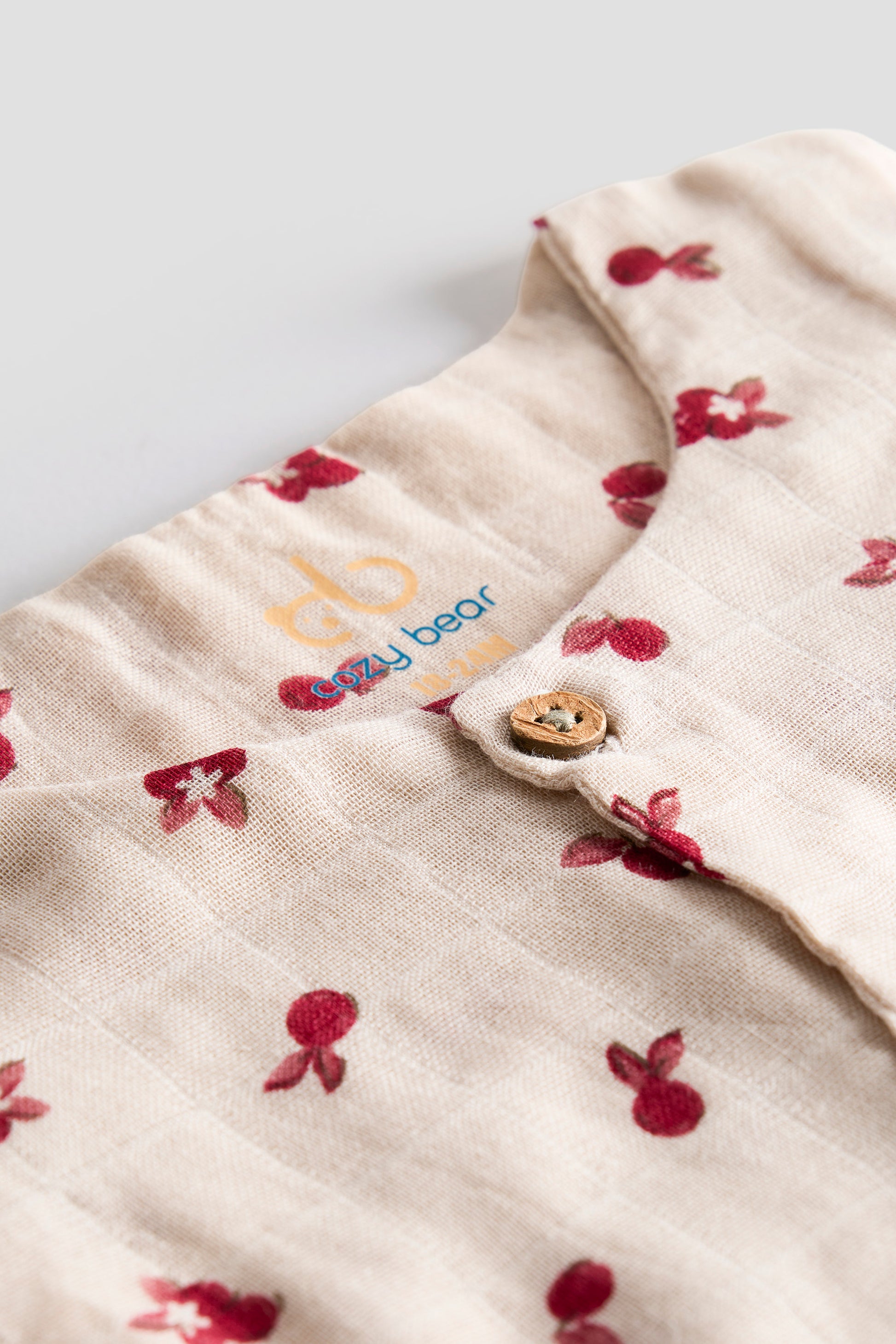 Close-up of a baby garment with floral patterns and a visible brand logo on a light background.
