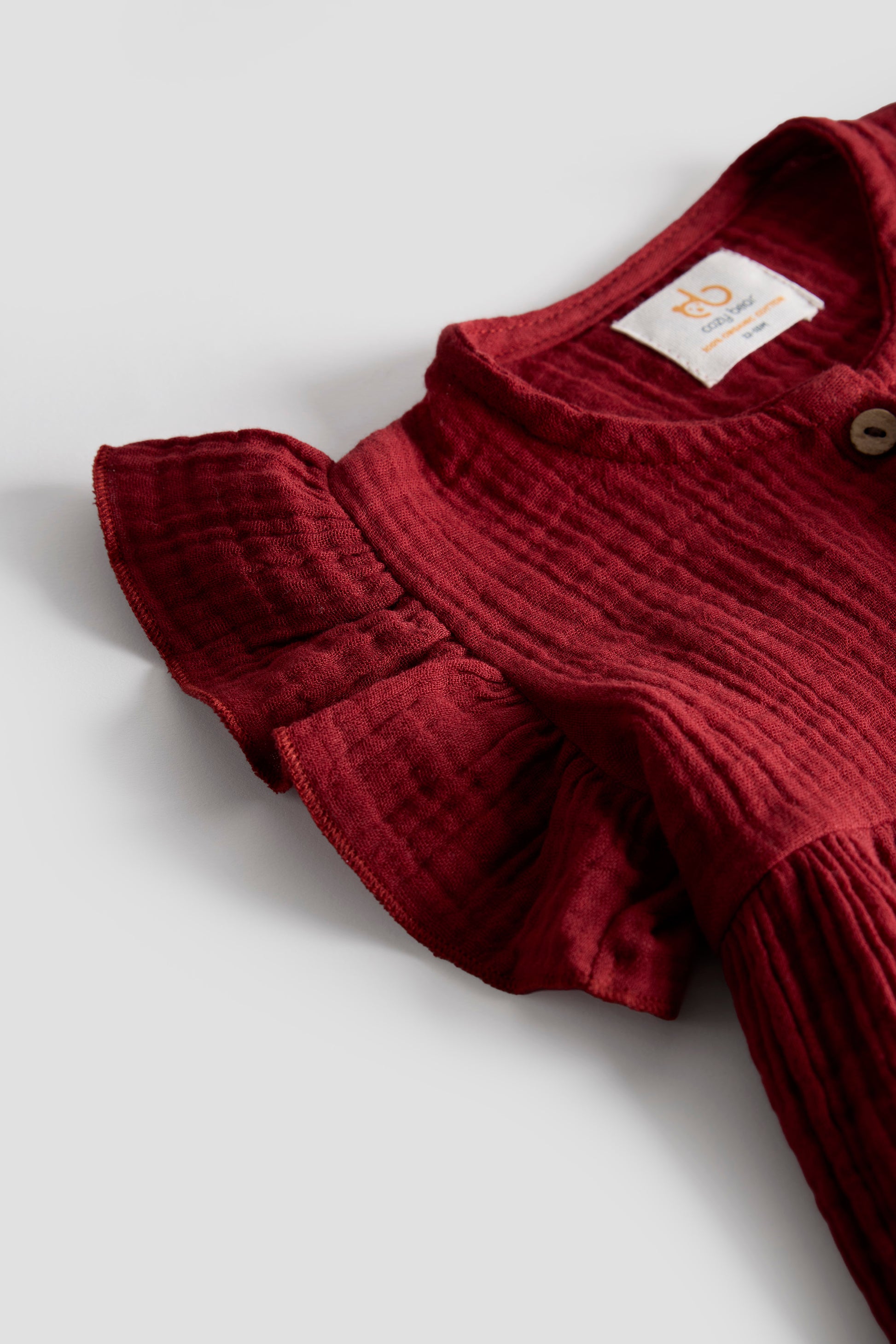 Maroon baby outfit with ruffled sleeves on a light gray background