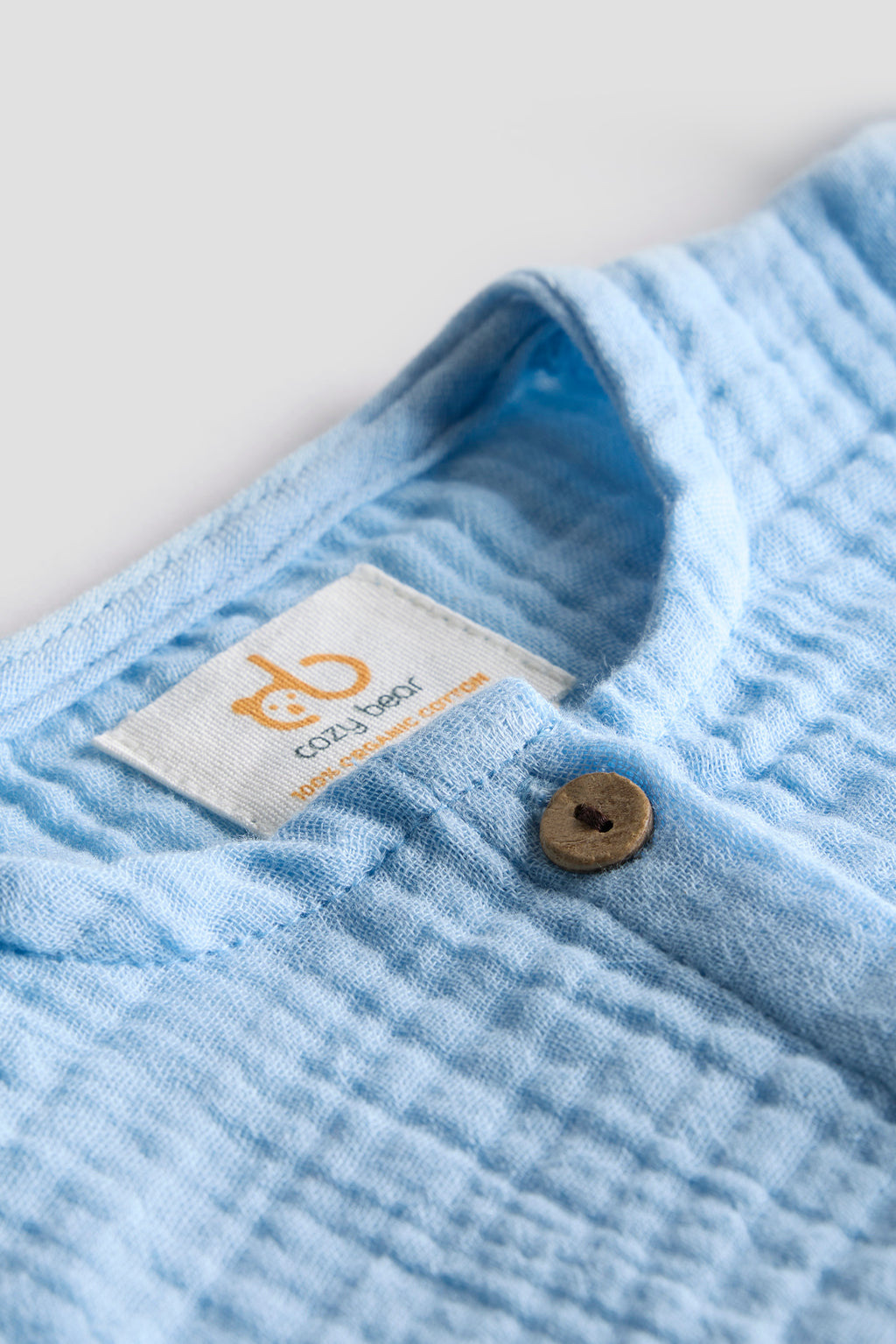 Close-up of a blue textured fabric with a brand label and button on a light gray background