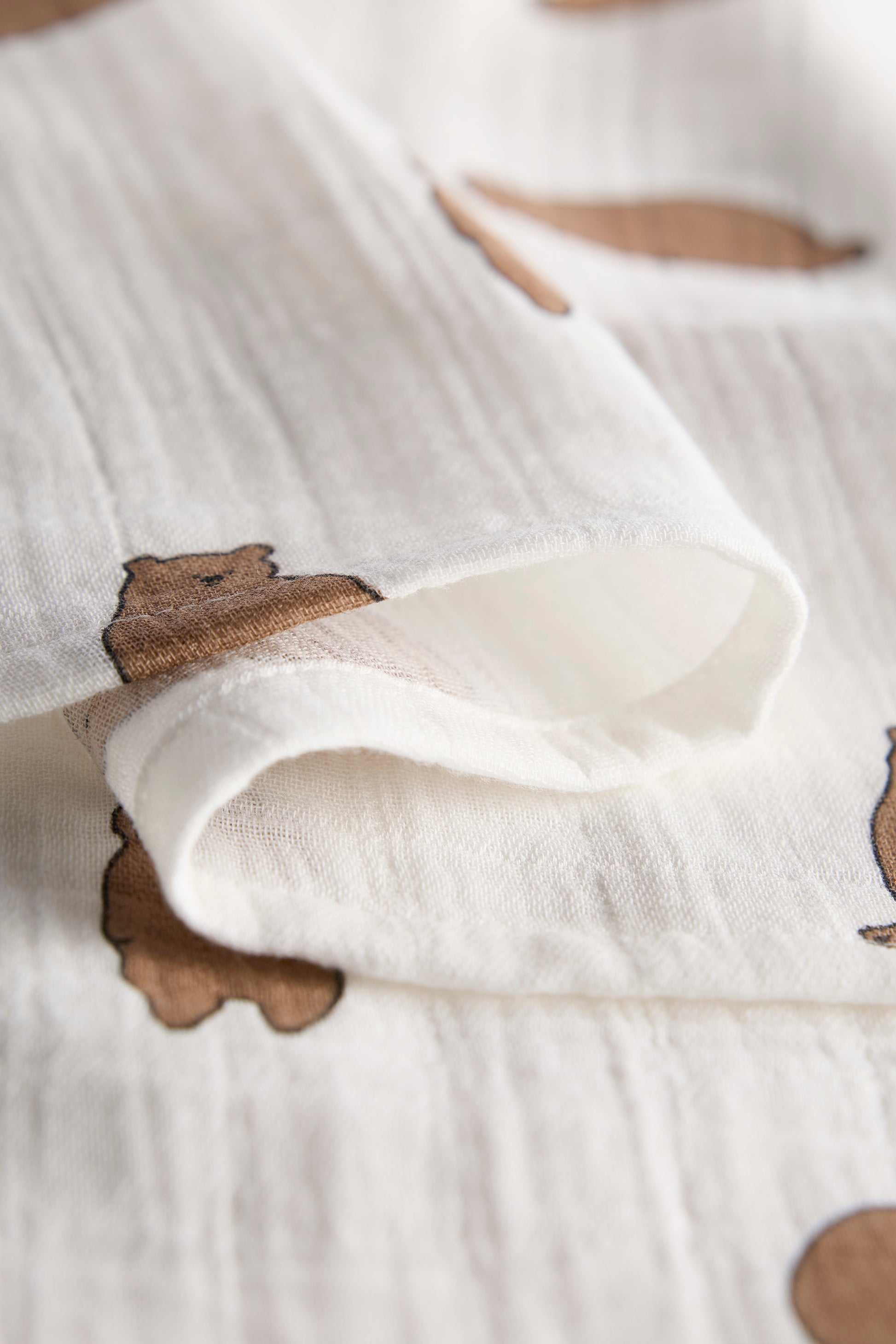 Close-up of a white fabric with brown bear shapes embroidered on it.