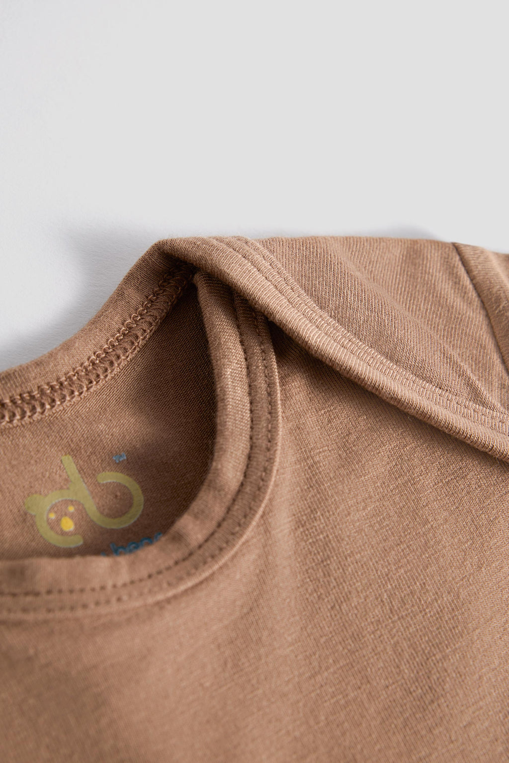 Close-up of a brown cotton t-shirt showing the inner neck label with a stylized 'db' logo, set against a plain light gray background.