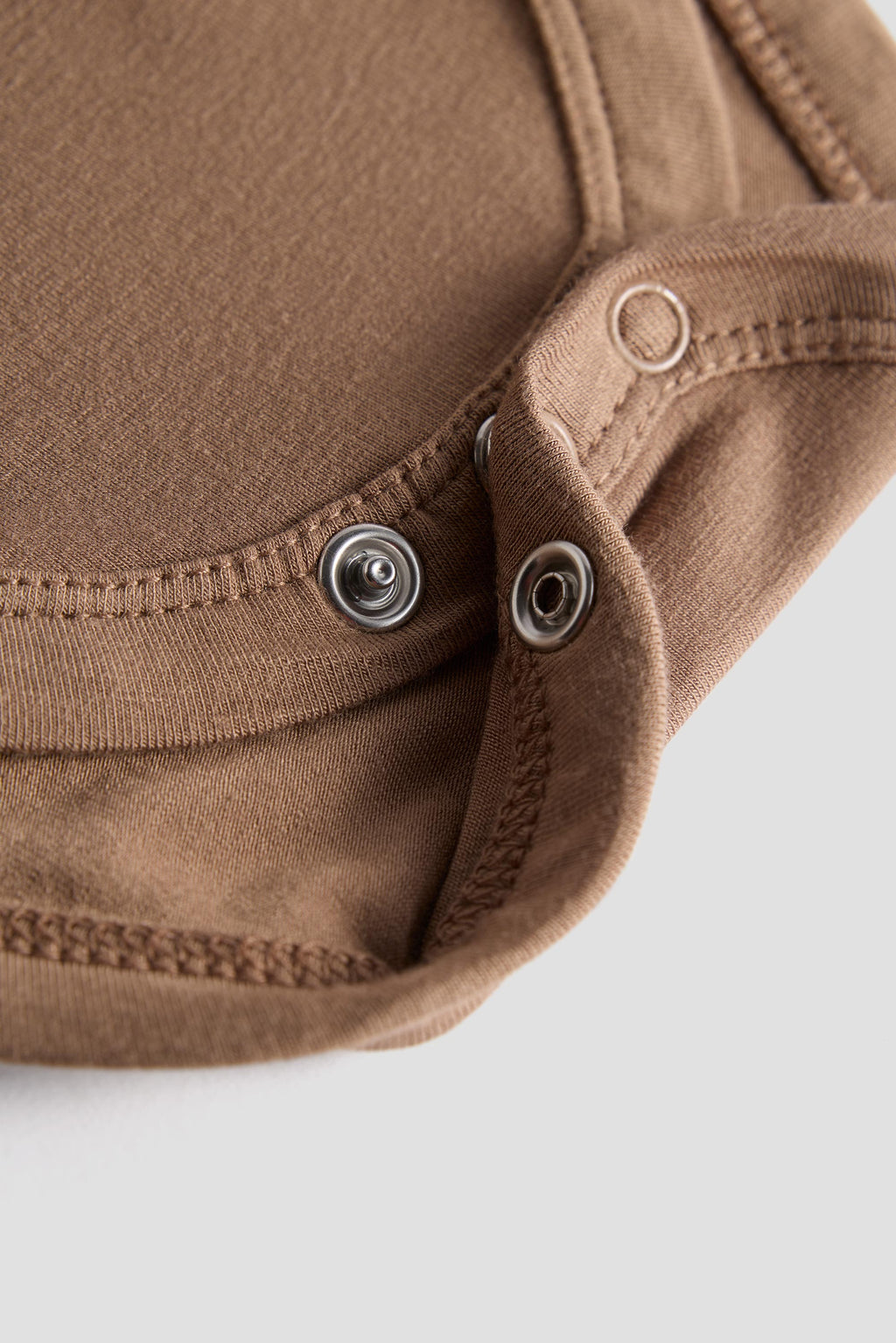 Close-up of a brown fabric garment with metal snap buttons and stitched edges on a light gray background.