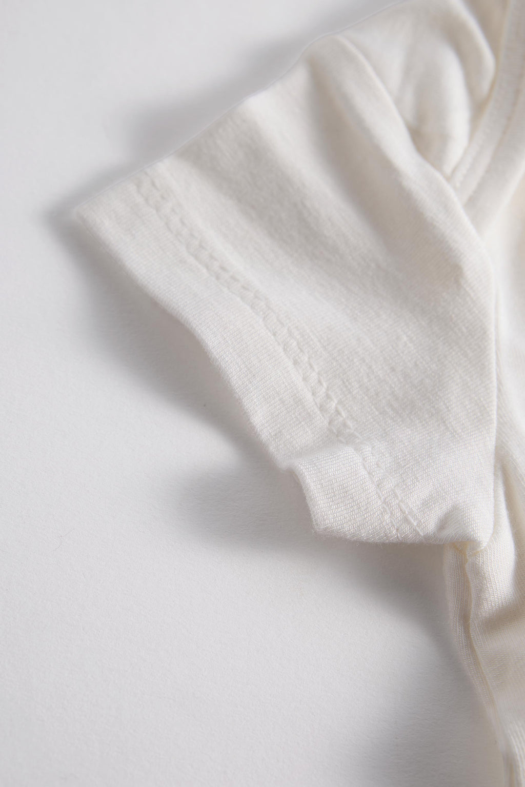 A close-up of a soft off-white or cream-colored fabric, showing the texture and fine stitching of a sleeve or cuff, set against a plain white background.