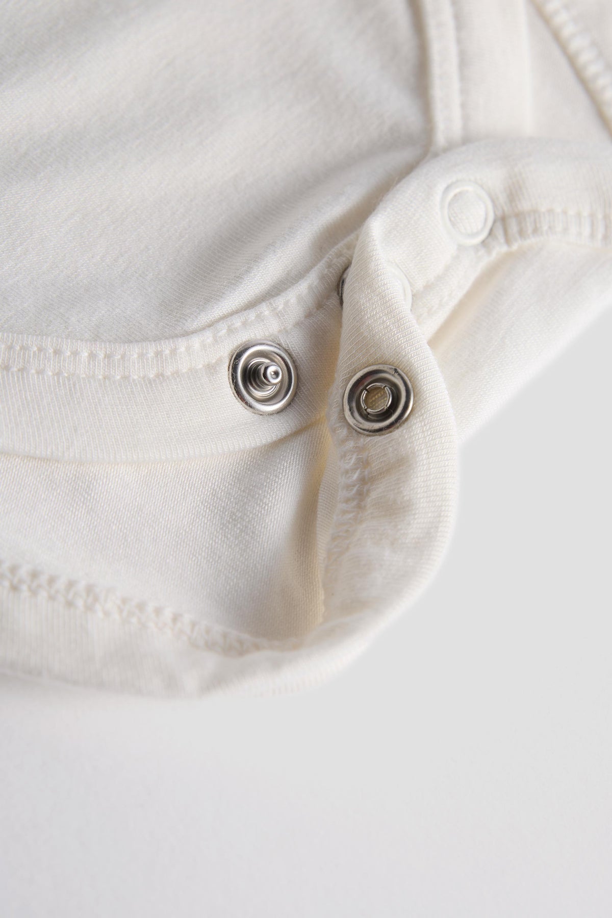Close-up of a white or off-white garment with two silver metal snap buttons on a plain light background.