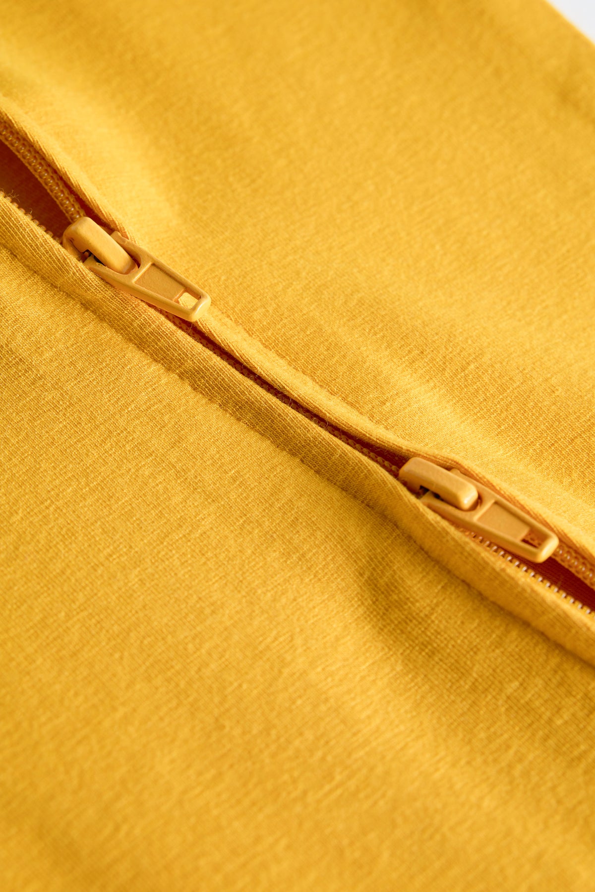 Close-up detail of a mustard yellow fabric item featuring a matching zipper with gold-toned metal teeth.