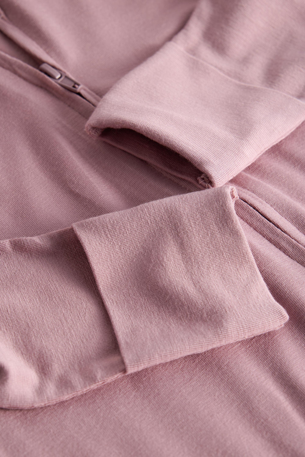 Close-up of a dusty pink zip-up hoodie showing the sleeve cuff, pocket, and zipper detail.