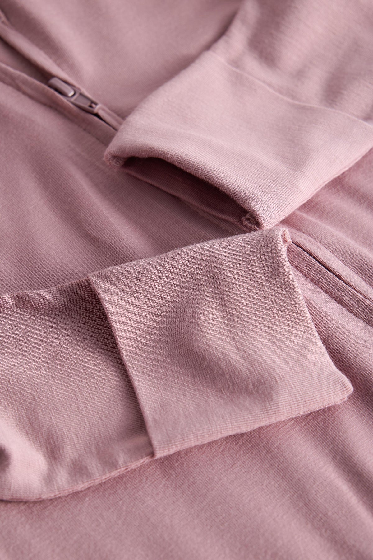 Close-up of a dusty pink zip-up hoodie showing the sleeve cuff, pocket, and zipper detail.