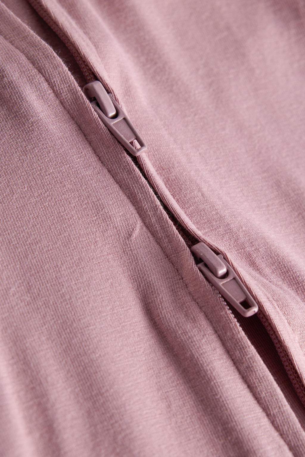Close-up of a dusty pink zippered garment, showing the textured fabric and silver-toned zipper pulls.