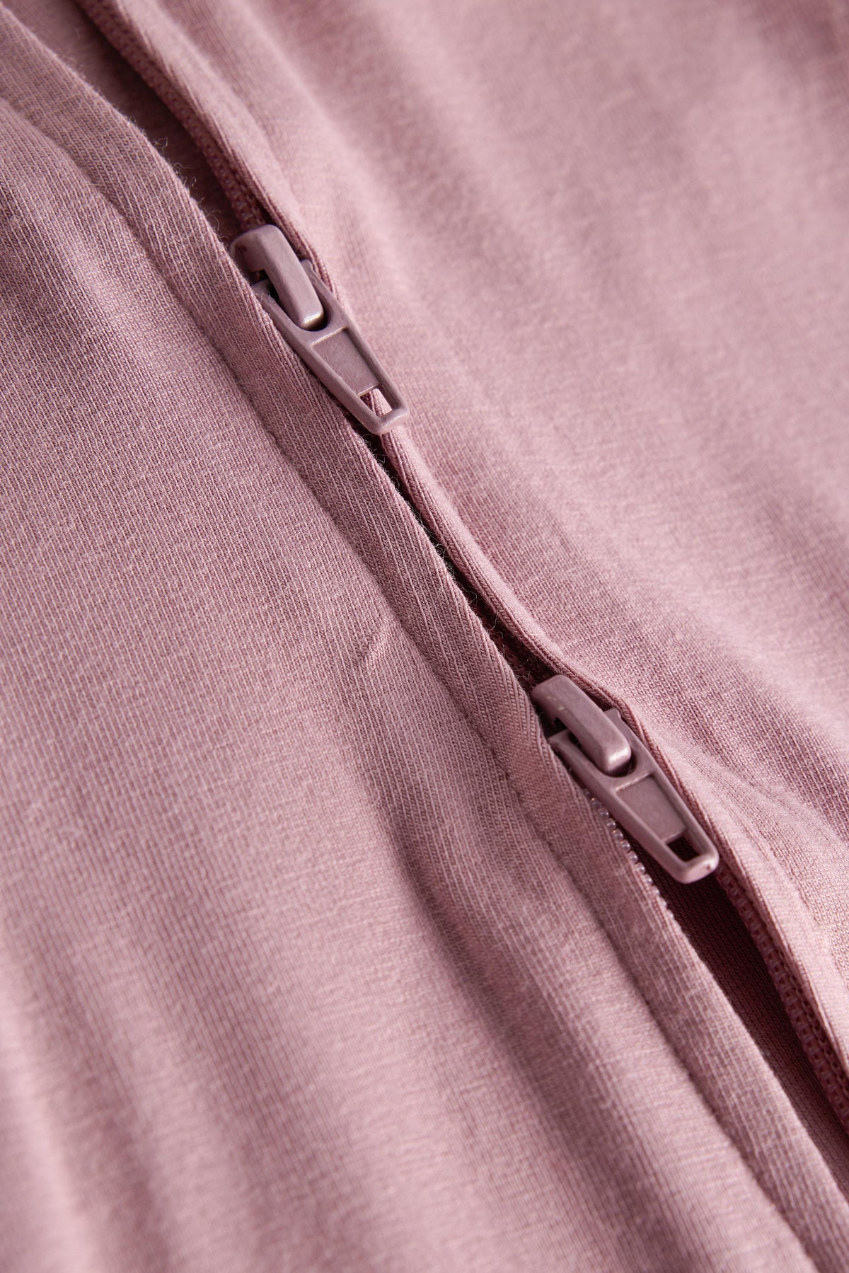 Close-up of a dusty pink zippered garment, showing the textured fabric and silver-toned zipper pulls.