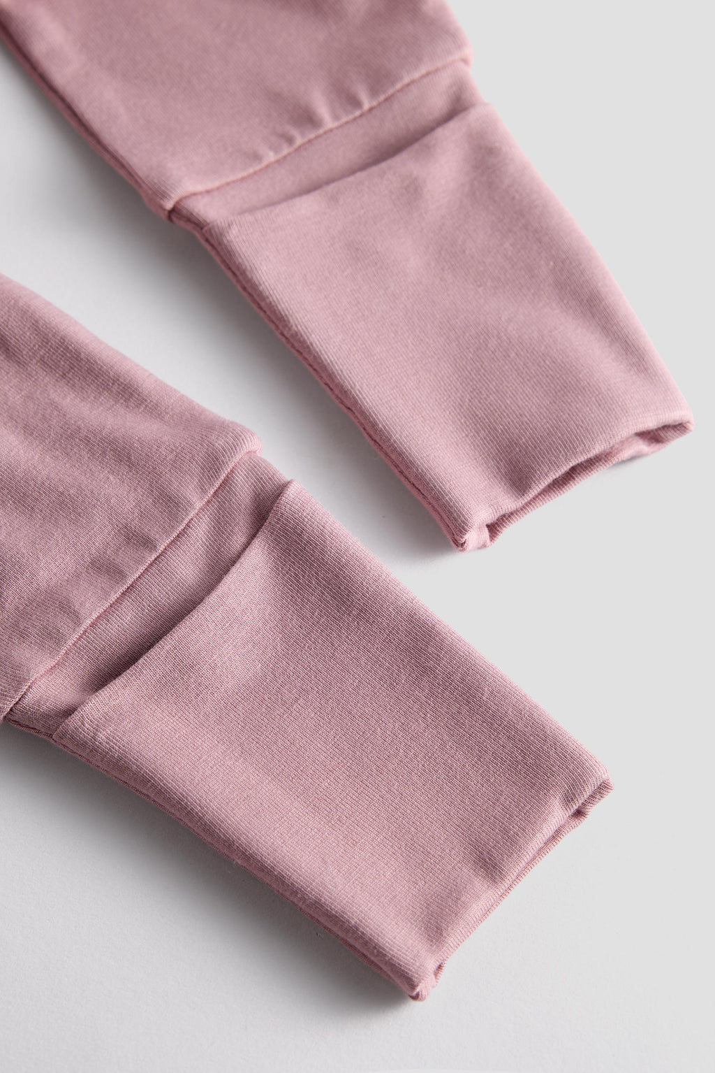Close-up of dusty pink fabric cuffs with visible stitching and folded edges on a light gray background.
