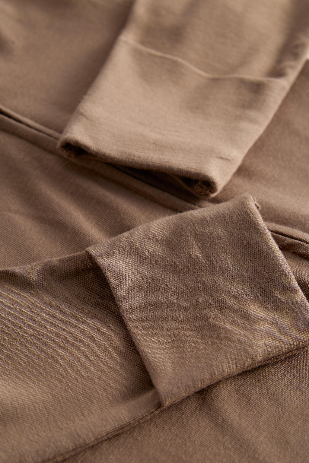 Close-up of a taupe brown knit fabric garment showing folded cuffs and soft texture.