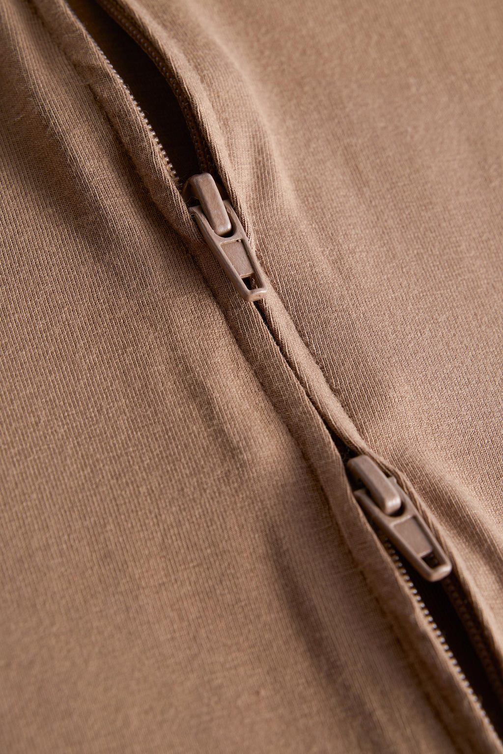 Close-up detail of a brown fabric garment with a zipper running diagonally across the frame.