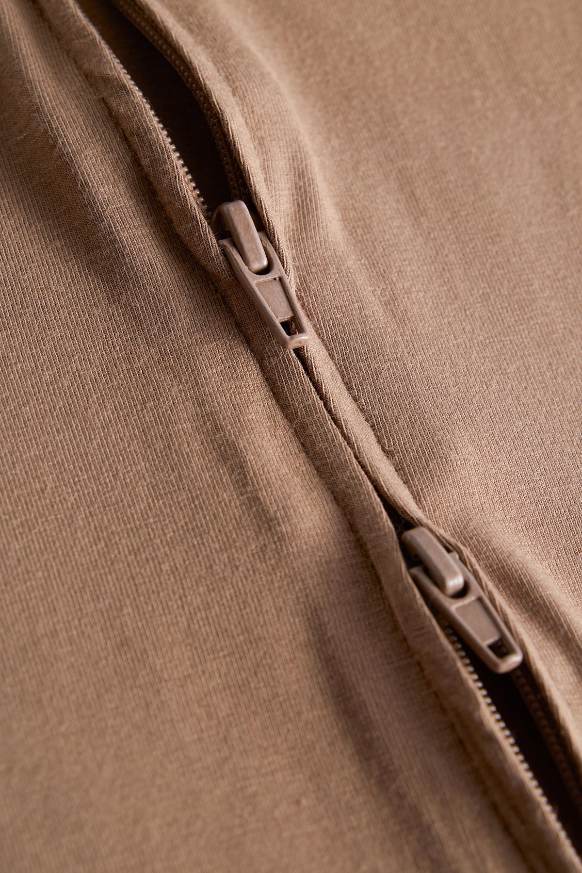 Close-up detail of a brown fabric garment with a zipper running diagonally across the frame.