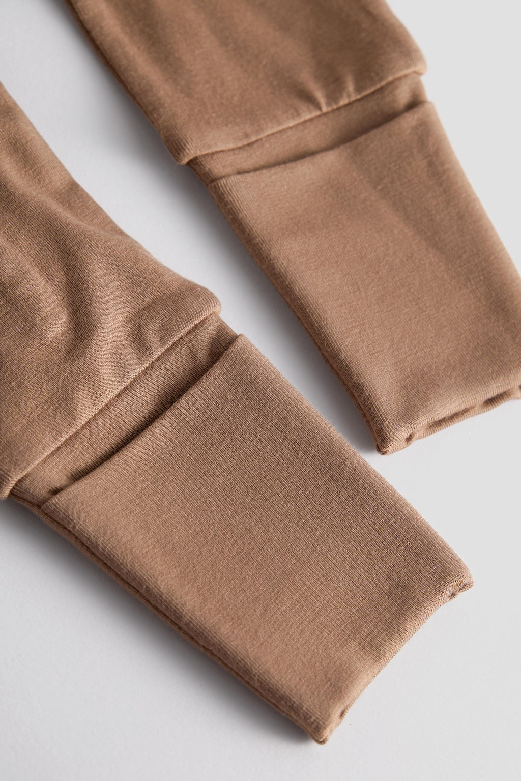 Close-up of tan fleece-lined cuffs on a pair of pants, showing the soft fabric texture and folded construction on a light gray background.