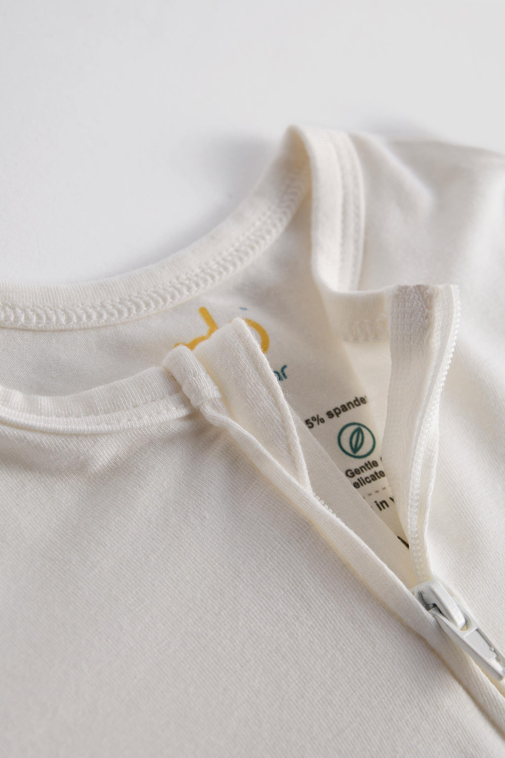 Close-up of a cream-colored zippered t-shirt showing the inner collar label with '5% spandex' and 'Gentle on skin' text.