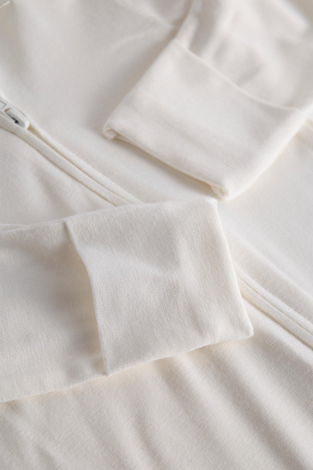 Close-up of a soft off-white fleece or knit garment with folded cuffs and a zipper detail, showing the fabric texture and color.