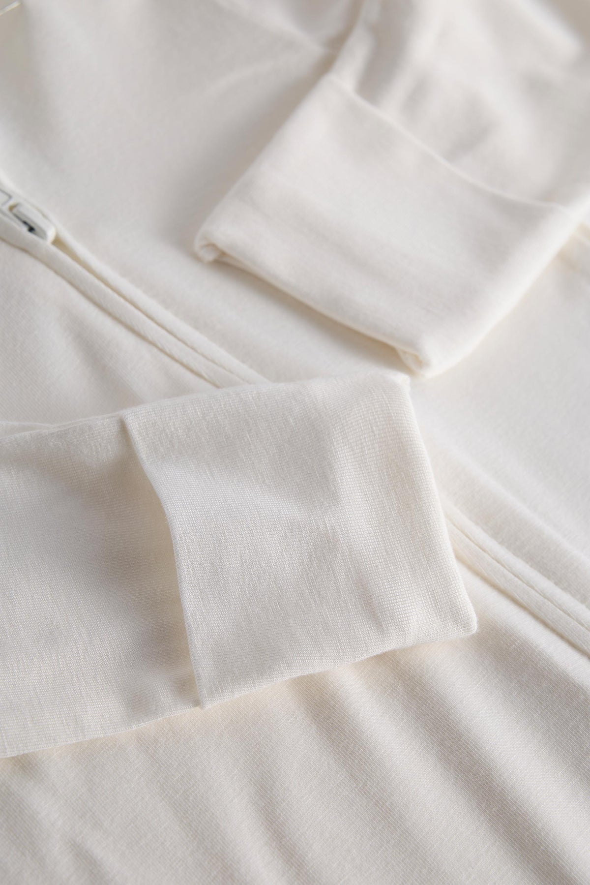 Close-up of a soft off-white fleece or knit garment with folded cuffs and a zipper detail, showing the fabric texture and color.