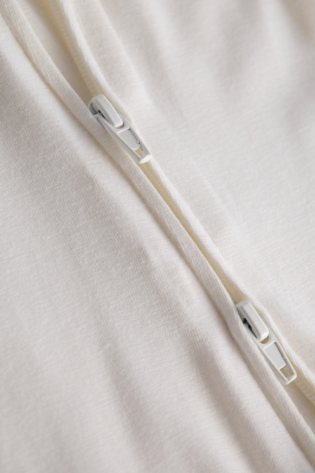 Close-up of a cream-colored fabric garment with a white zipper running diagonally across the frame.