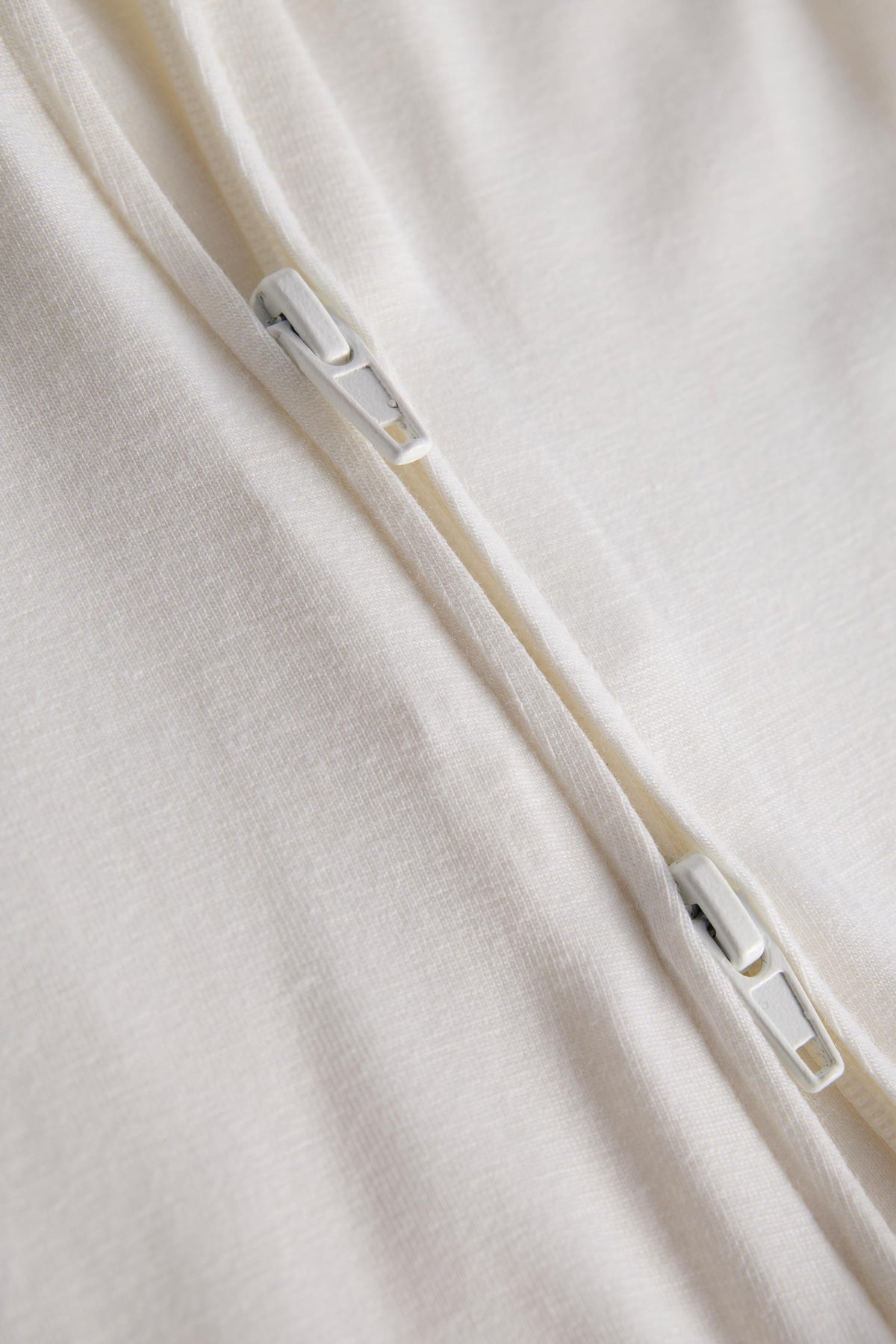 Close-up of a cream-colored fabric garment with a white zipper running diagonally across the frame.
