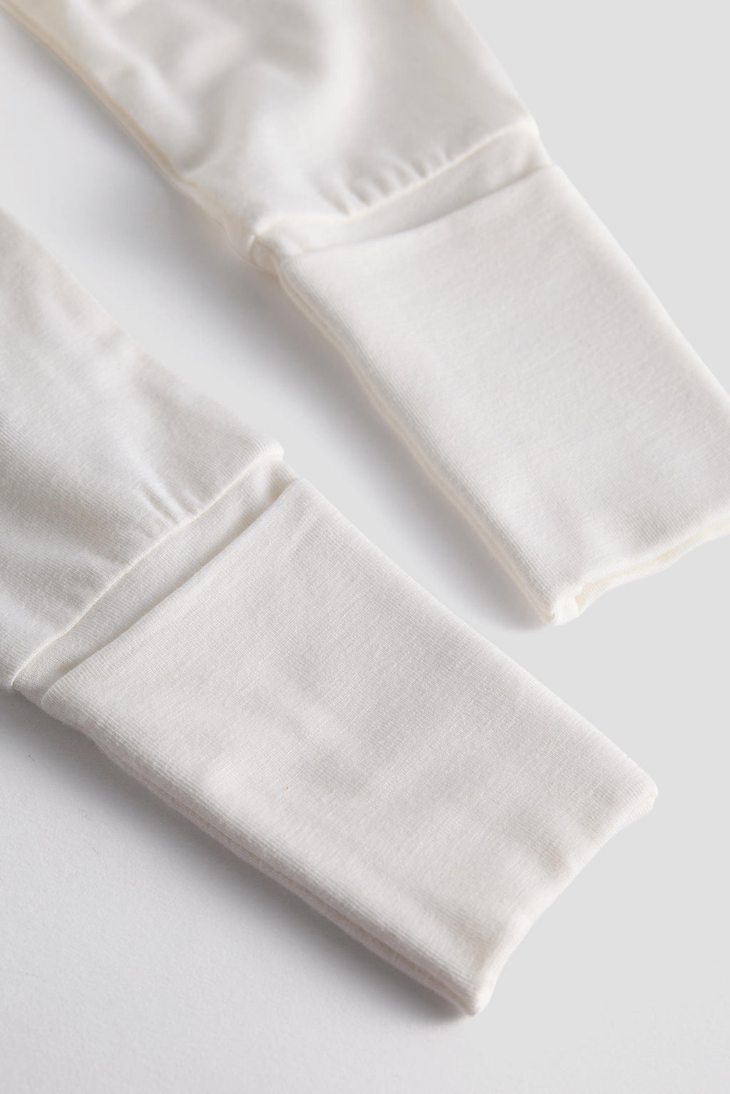Close-up of a pair of off-white or cream knit pants or leggings cuffs laid flat on a light neutral background.