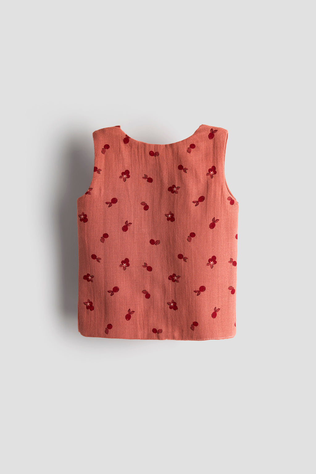 Pink sleeveless top with cherry pattern on a light gray background