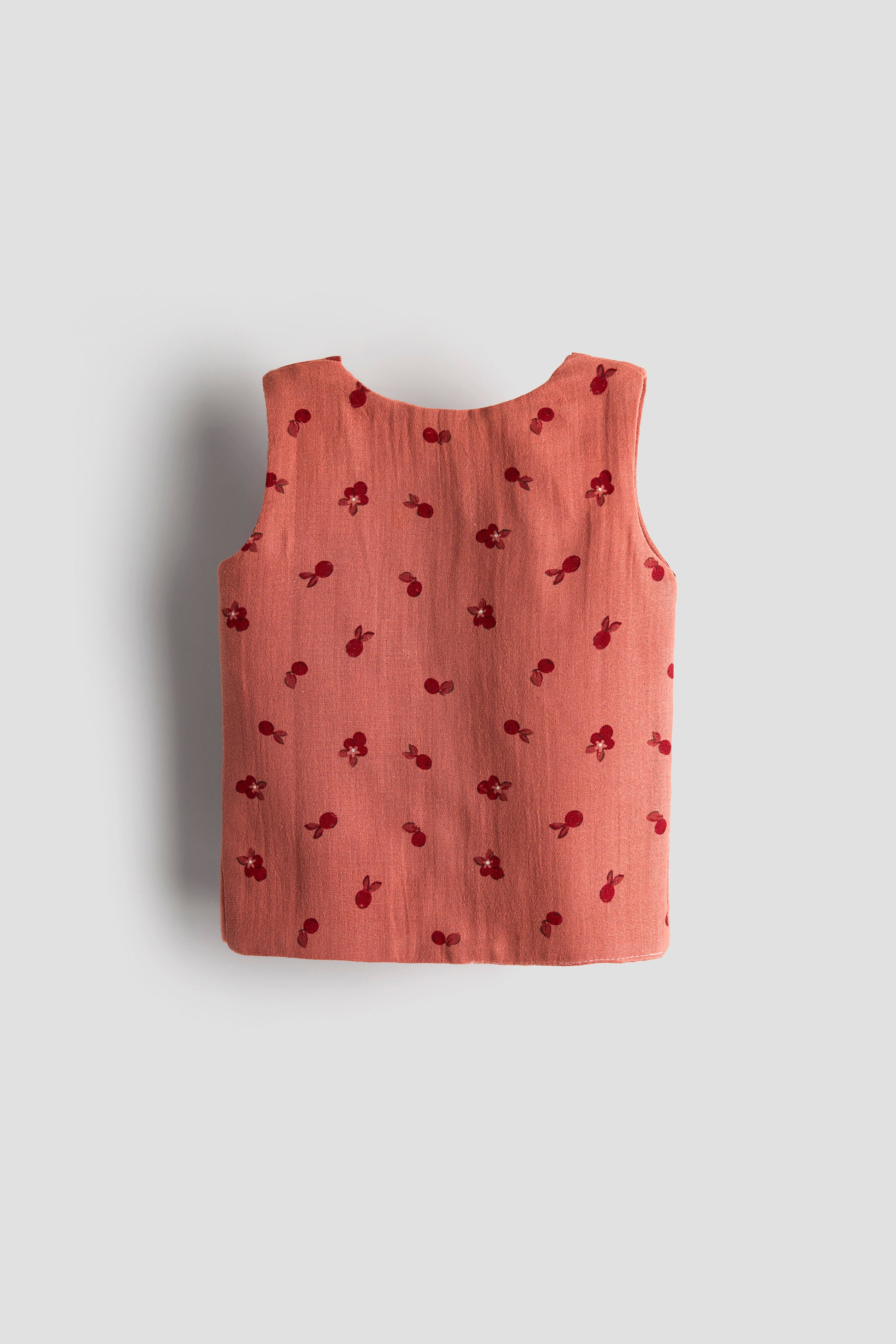 Pink sleeveless top with cherry pattern on a light gray background