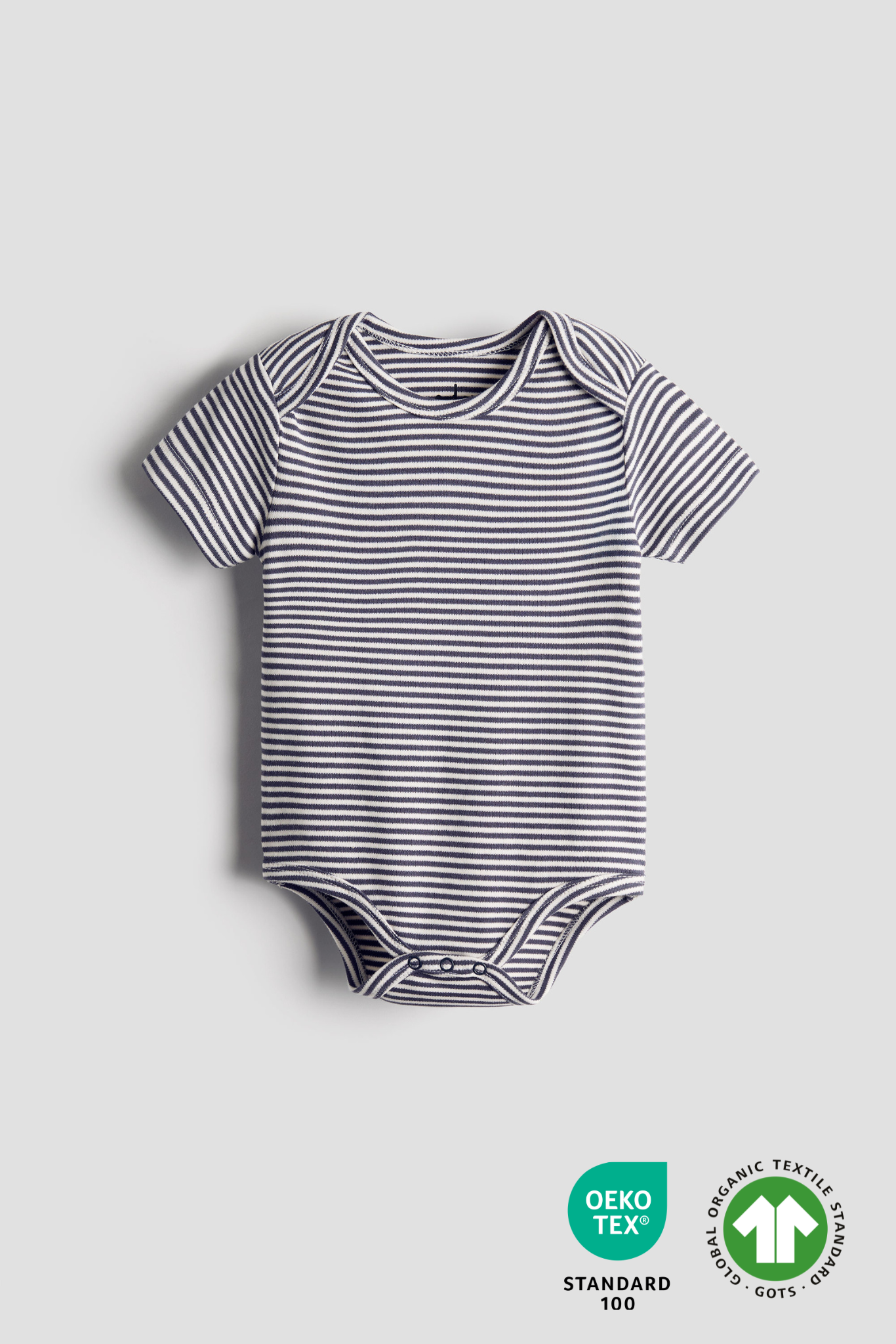 Striped baby bodysuit with organic textile standards logo on a light gray background