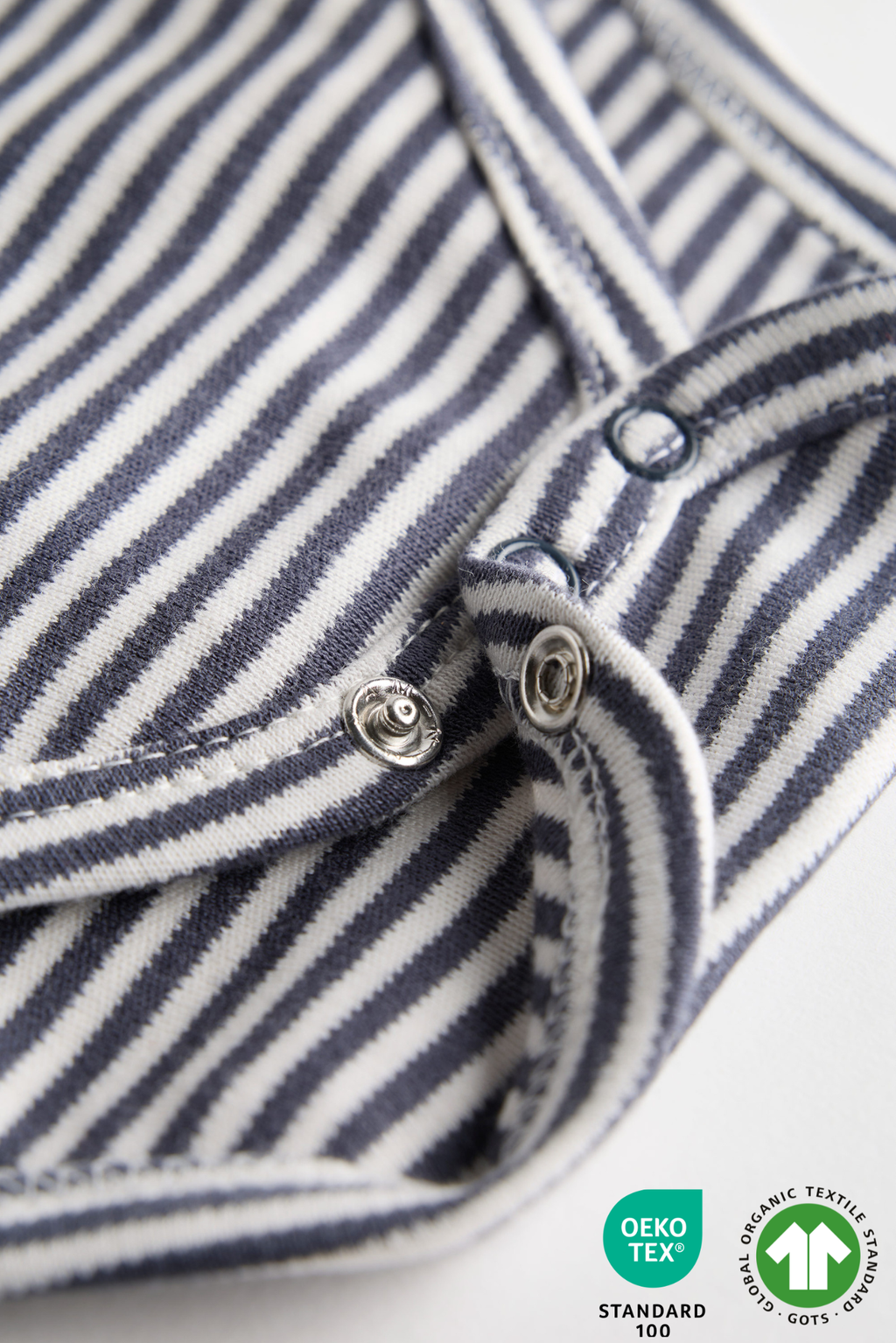 Close-up of a blue and white striped shirt with buttons, featuring Oeko-Tex and GOTS logos.