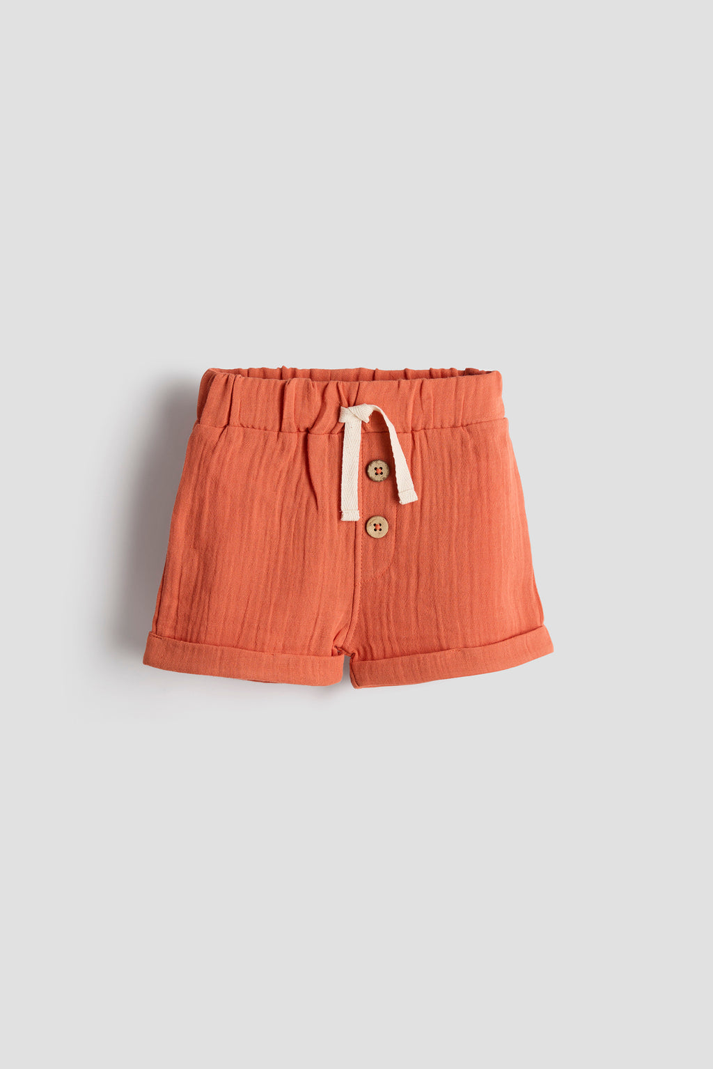 Orange shorts with buttons and drawstring on a light gray background
