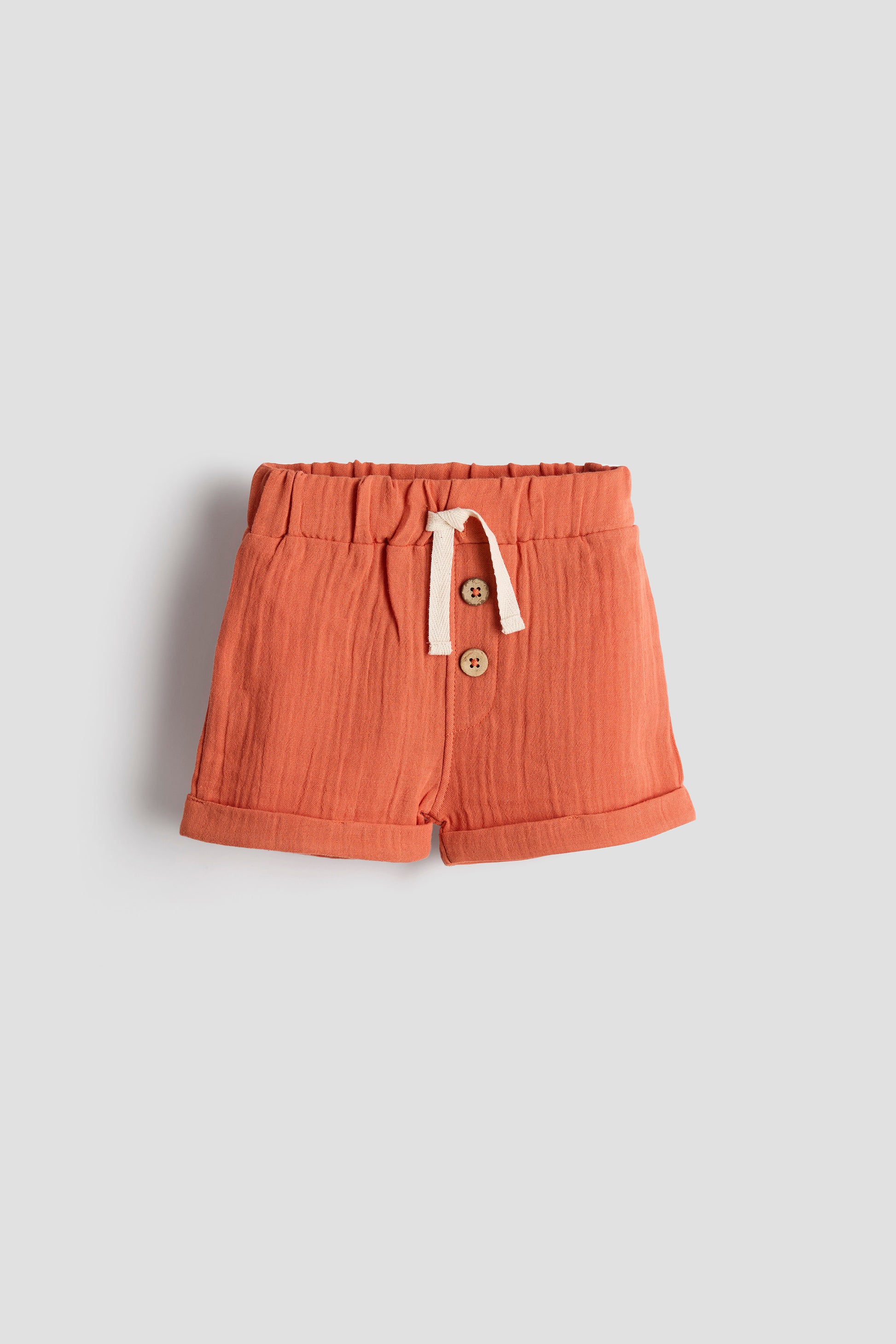Orange shorts with buttons and drawstring on a light gray background