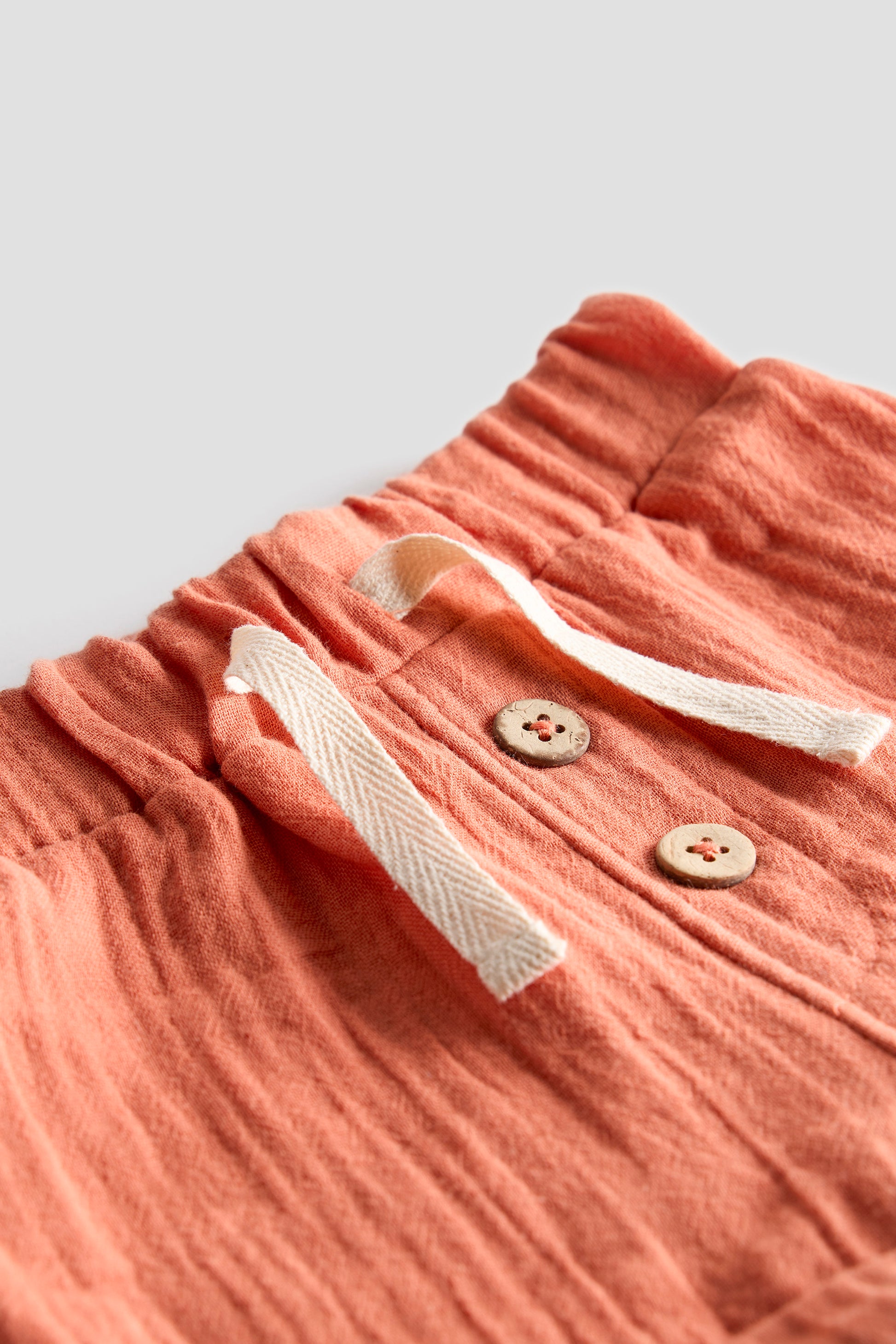 Pink pants with a drawstring and buttons on a light gray background