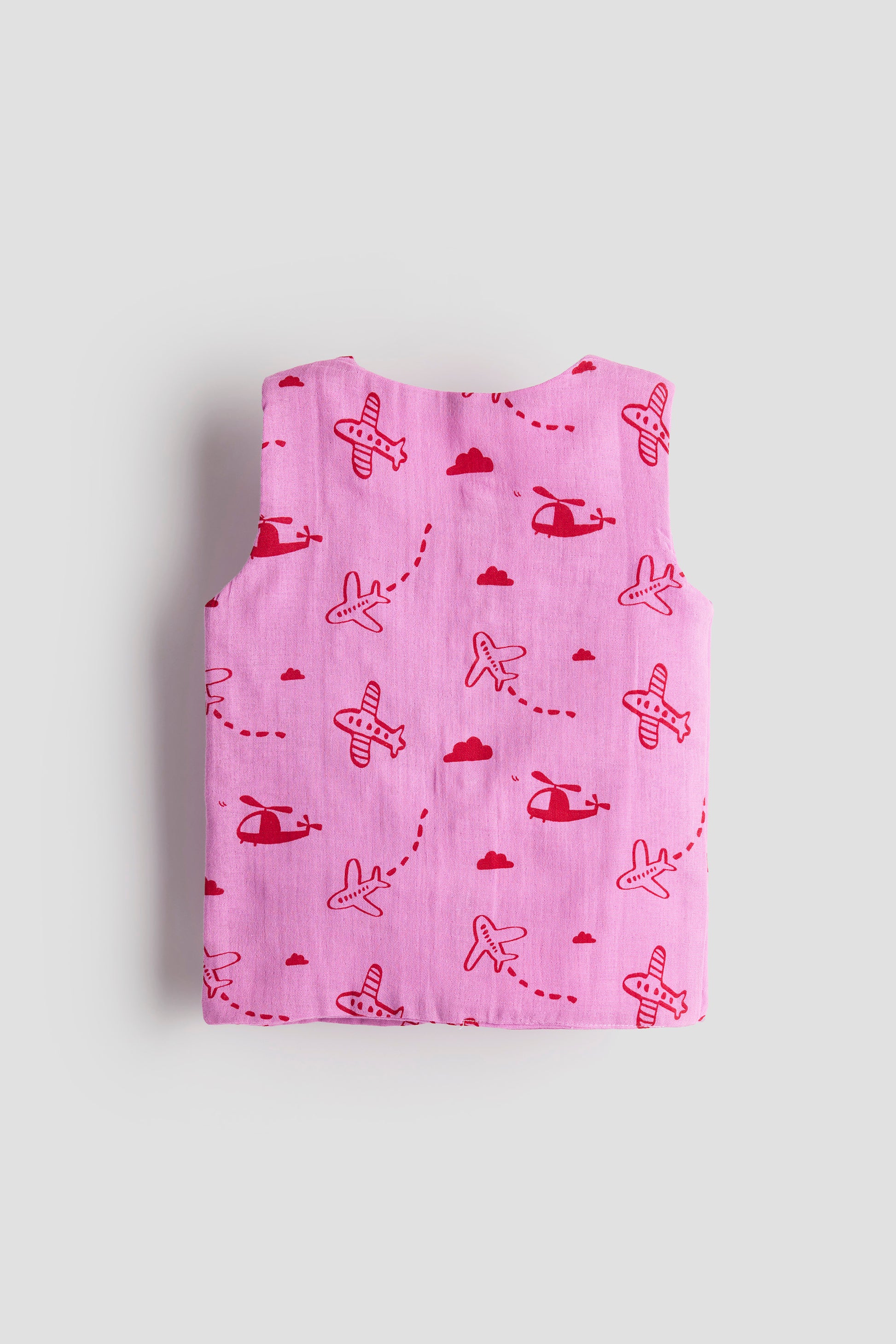 Folded pink blanket with red airplane and helicopter patterns on a light gray background