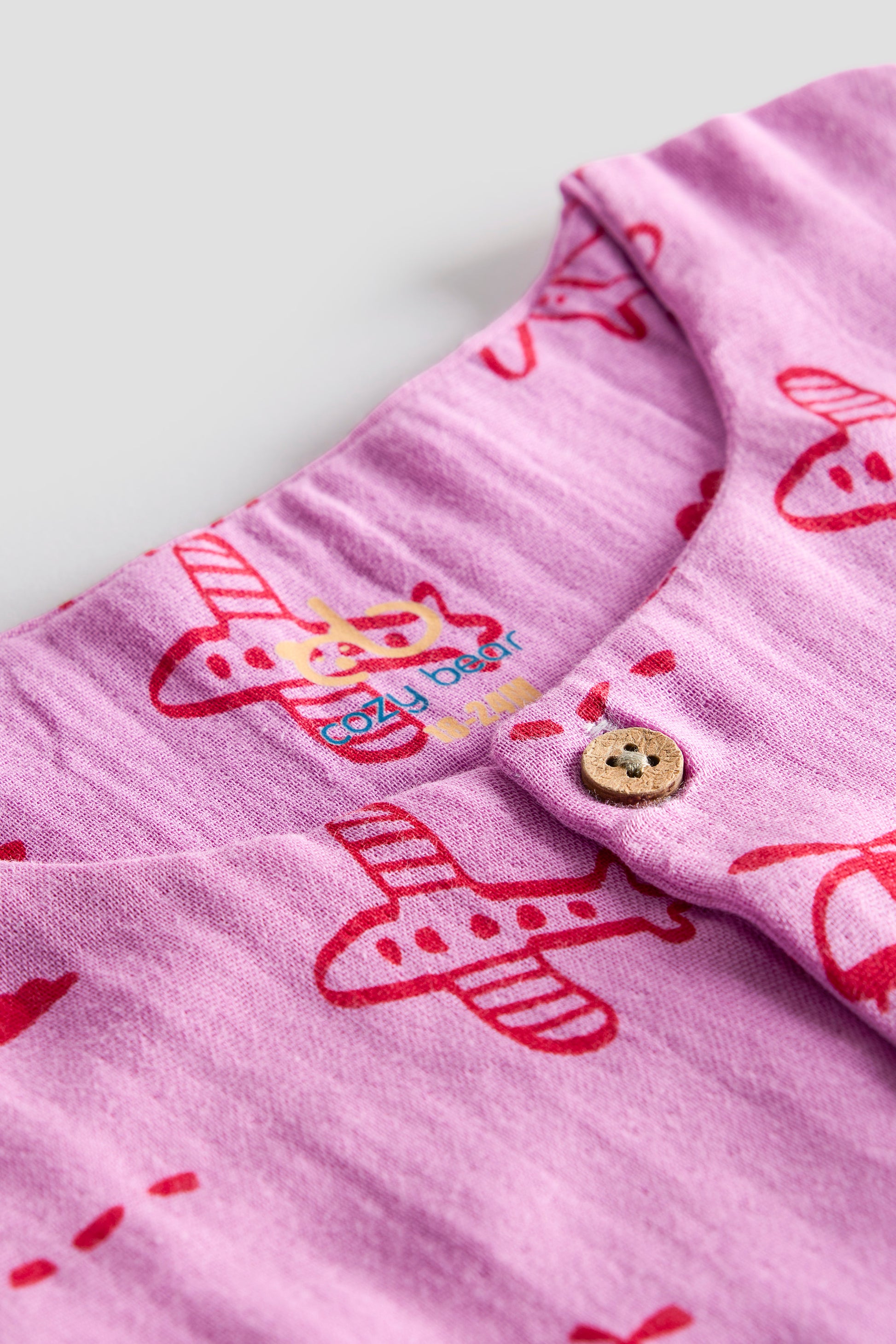 Close-up of a pink fabric with red airplane patterns and a button on a light purple background