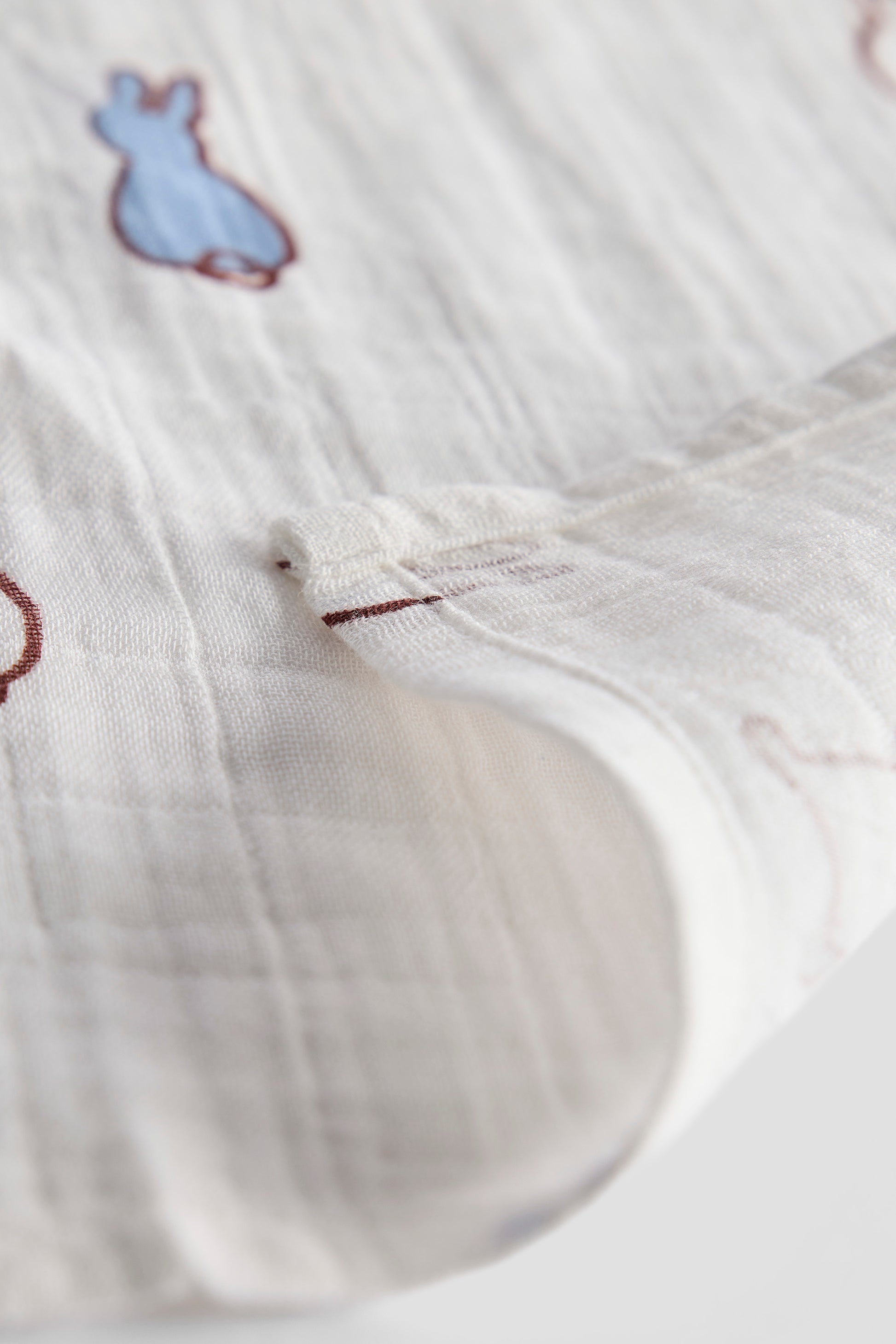 Close-up of white fabric with embroidered bunny ears and a button, on a light gray background.