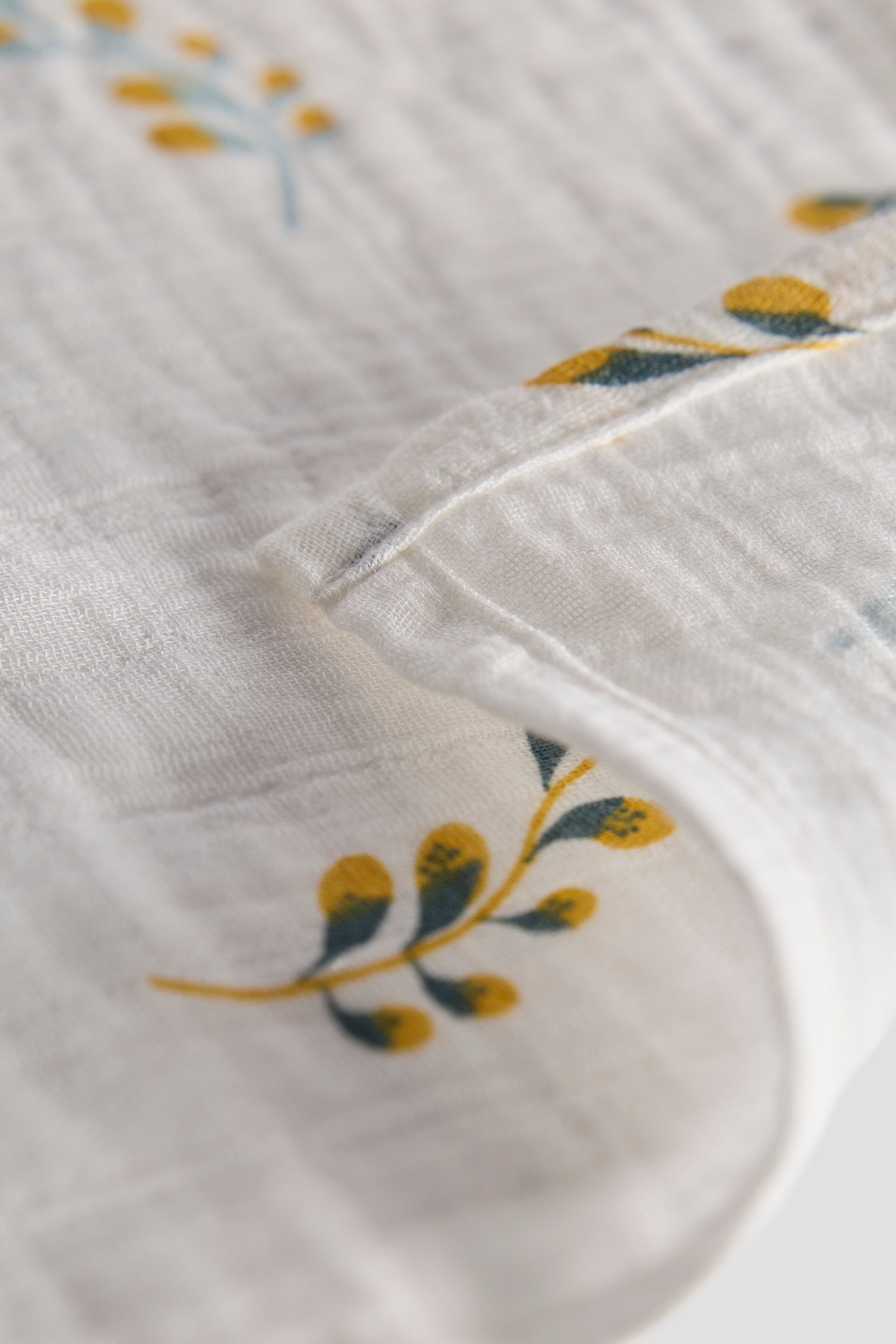 Close-up of a white fabric with embroidered yellow flowers on a light gray background
