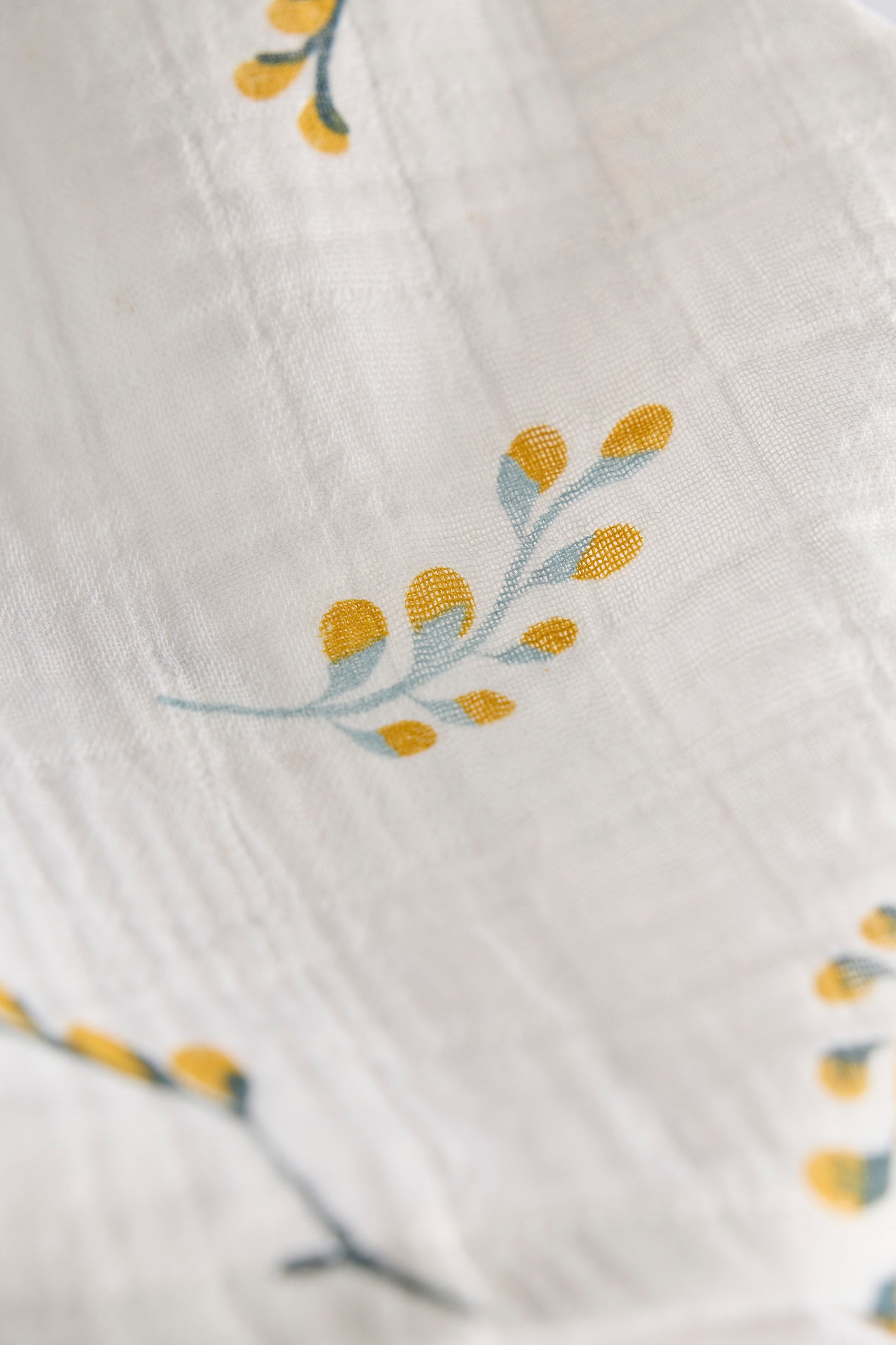 Close-up of a textured fabric with embroidered yellow flowers on a white background