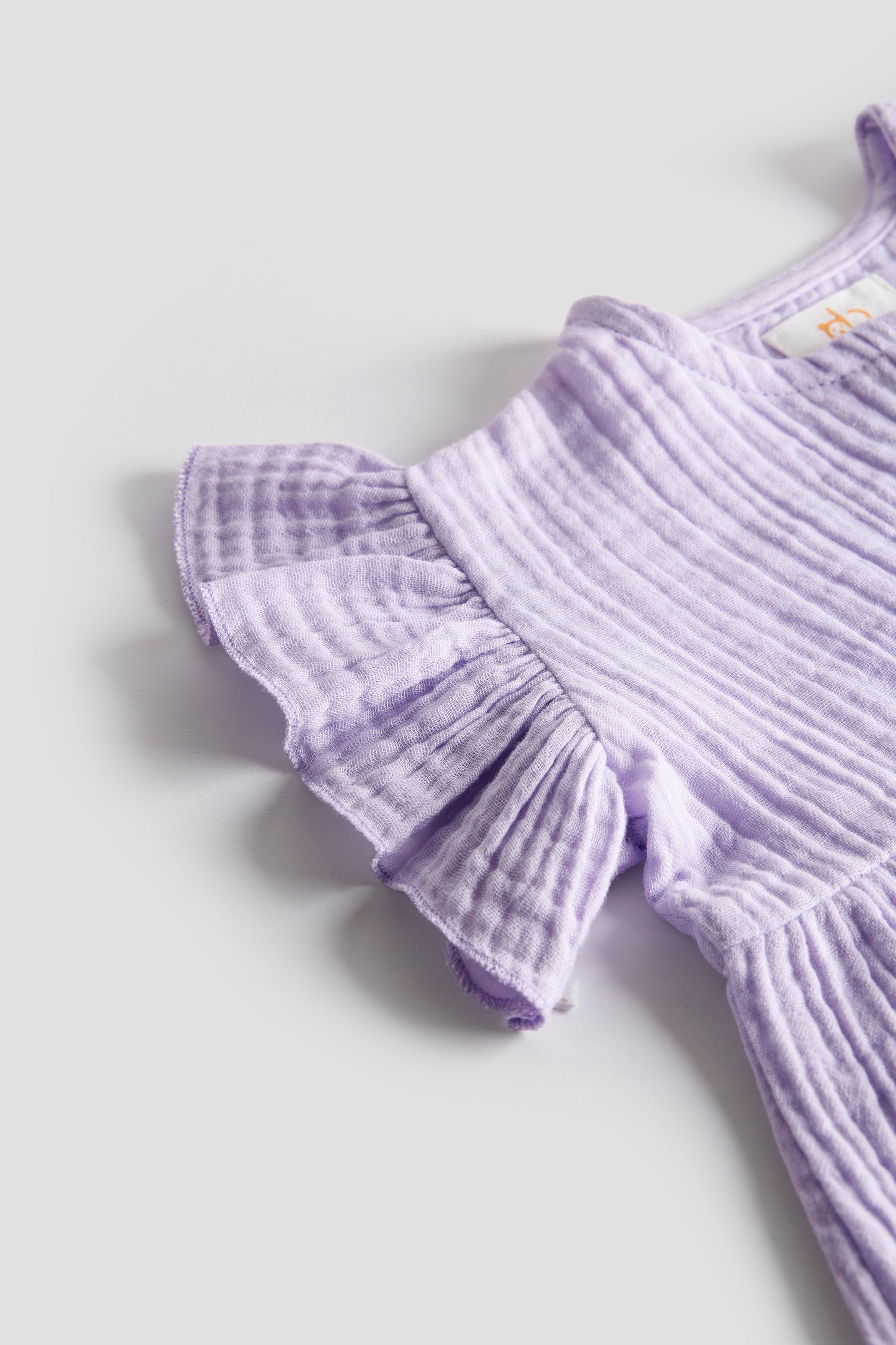 Lavender ribbed romper with ruffled details on a light gray background