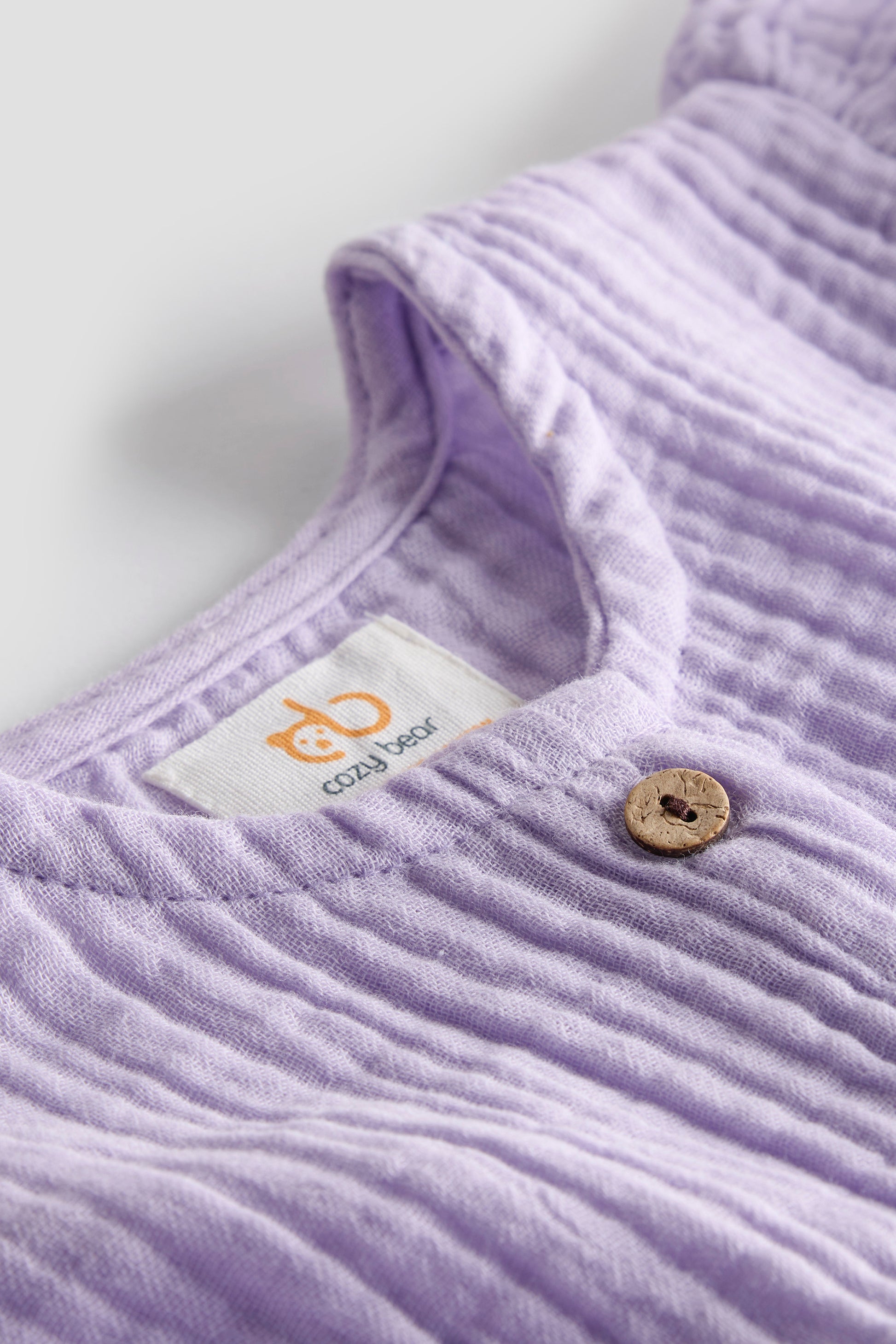 Close-up of a purple textured garment with a button and 'czzy bear' label.