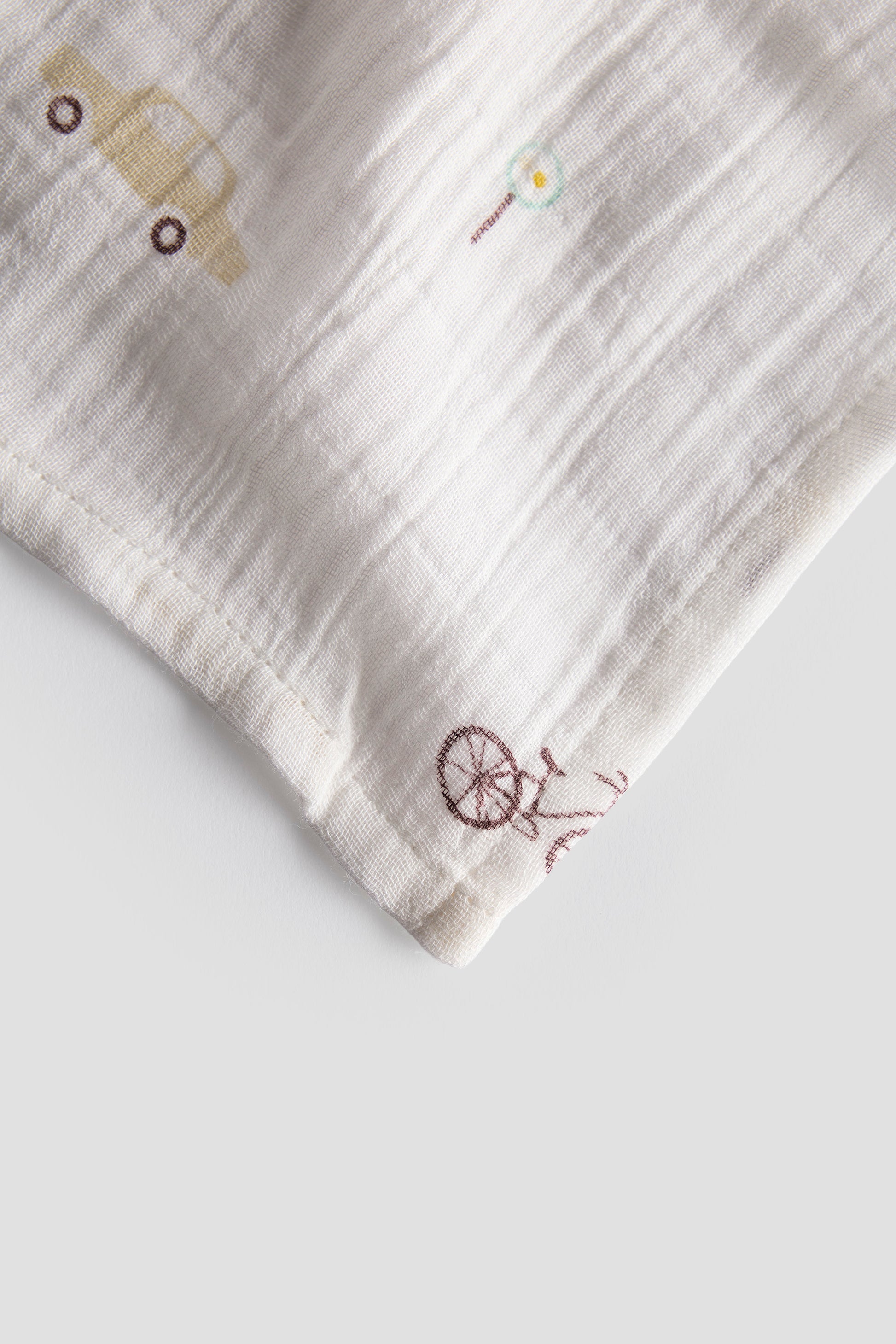 Folded fabric with embroidered car and bicycle designs on a light background