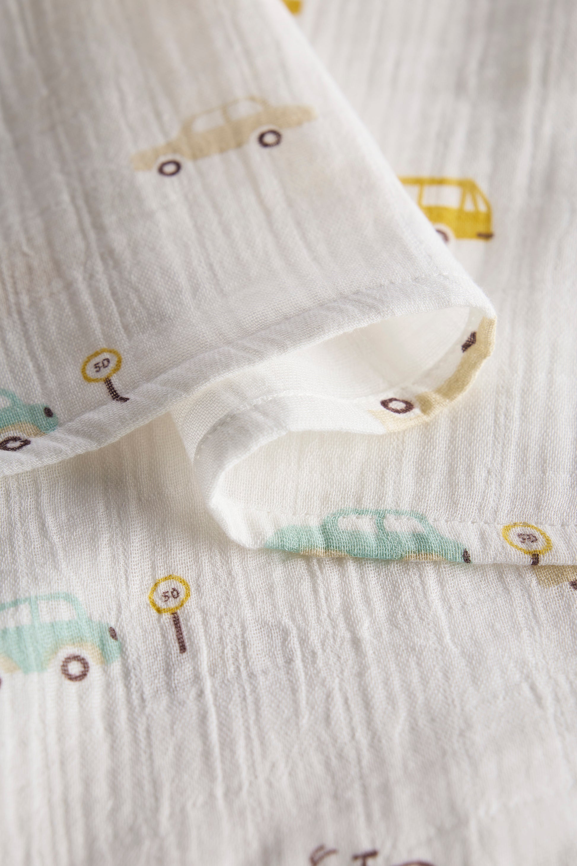 Close-up of white fabric with small vehicle patterns, including cars and trucks.