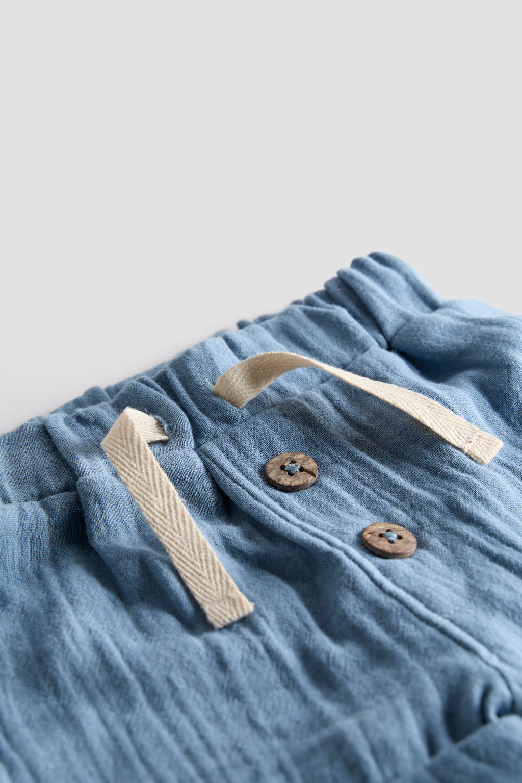 Blue fabric with buttons and a strap on a light gray background