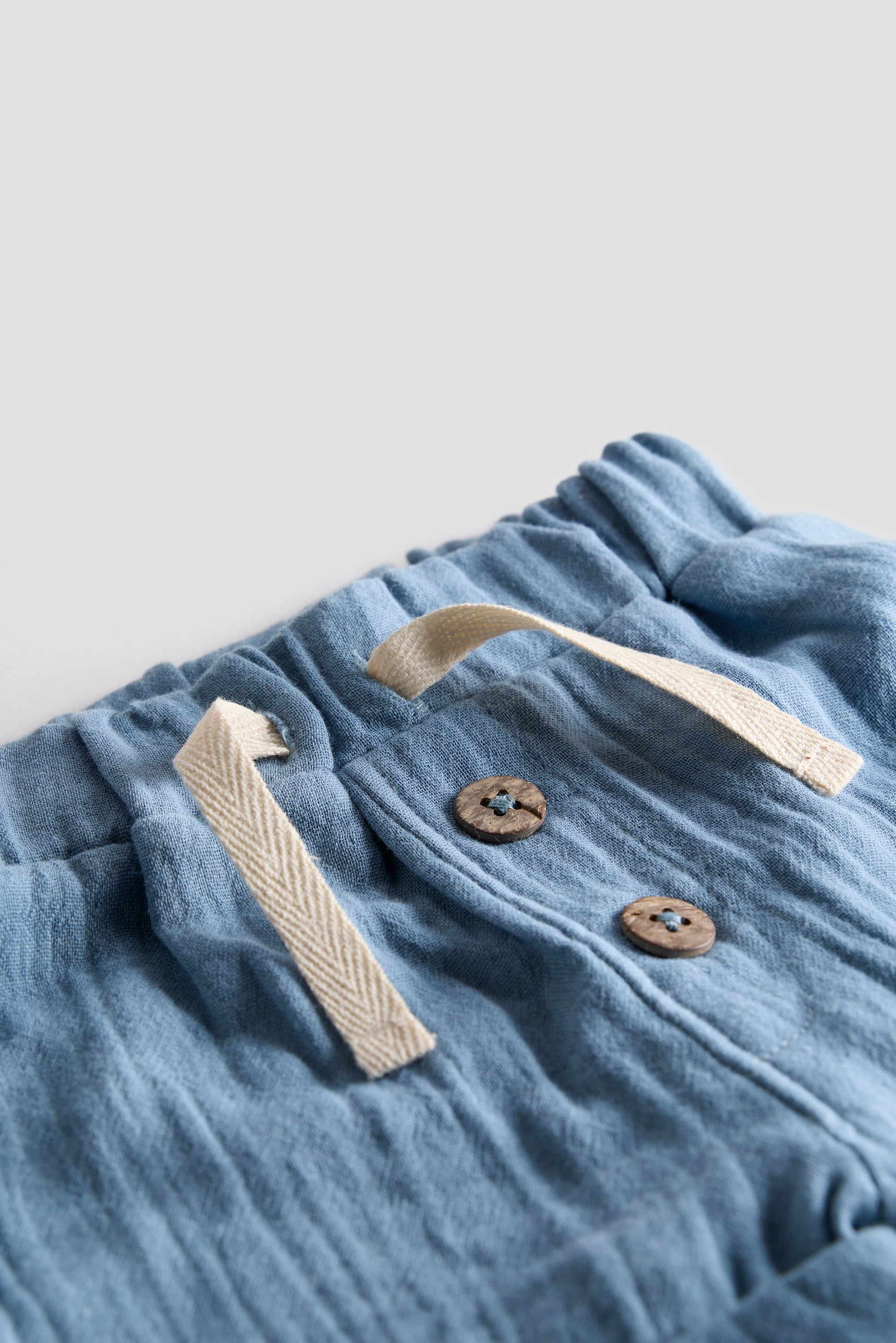 Blue fabric with buttons and a strap on a light gray background