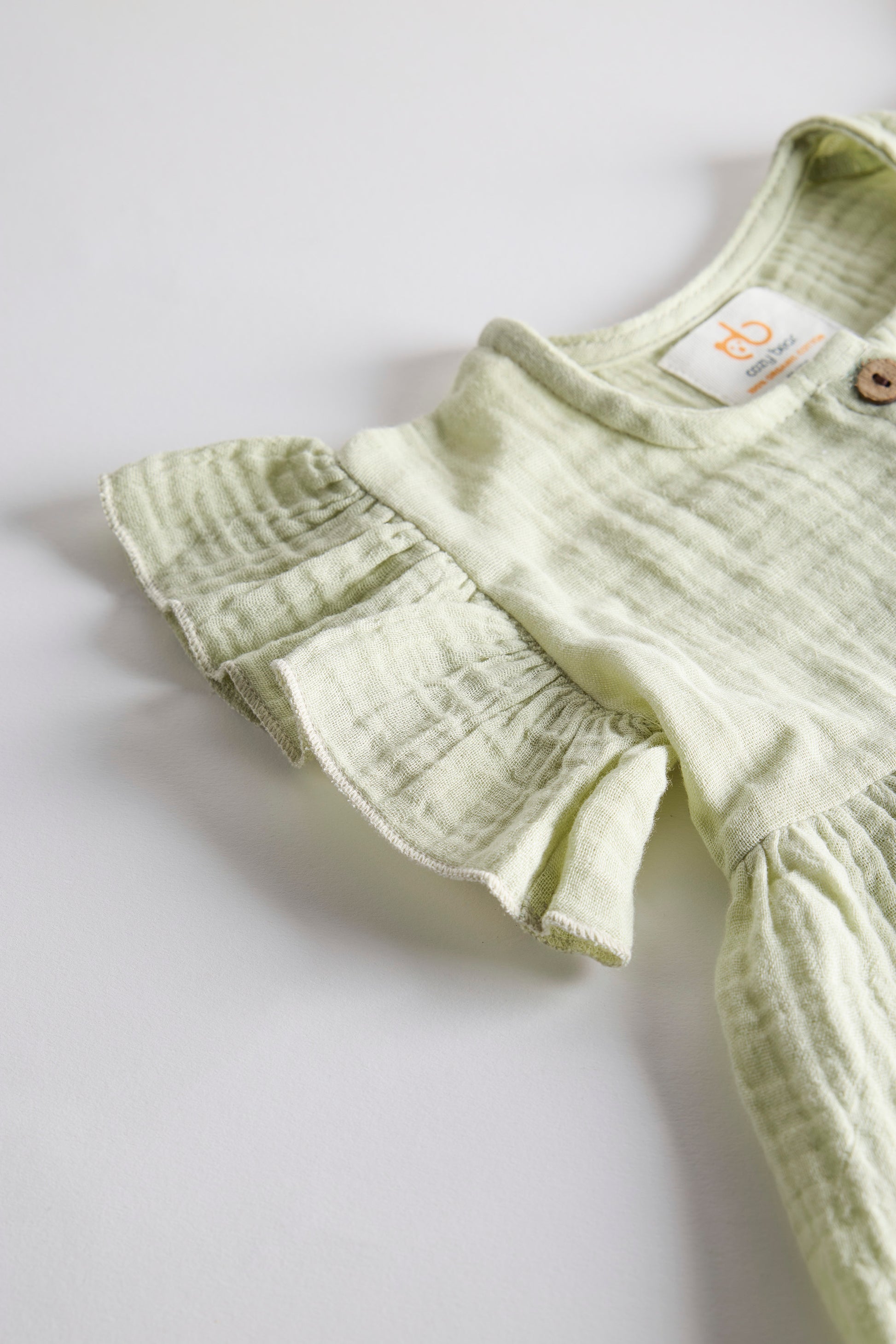 Light green baby romper with ruffled details on a white background