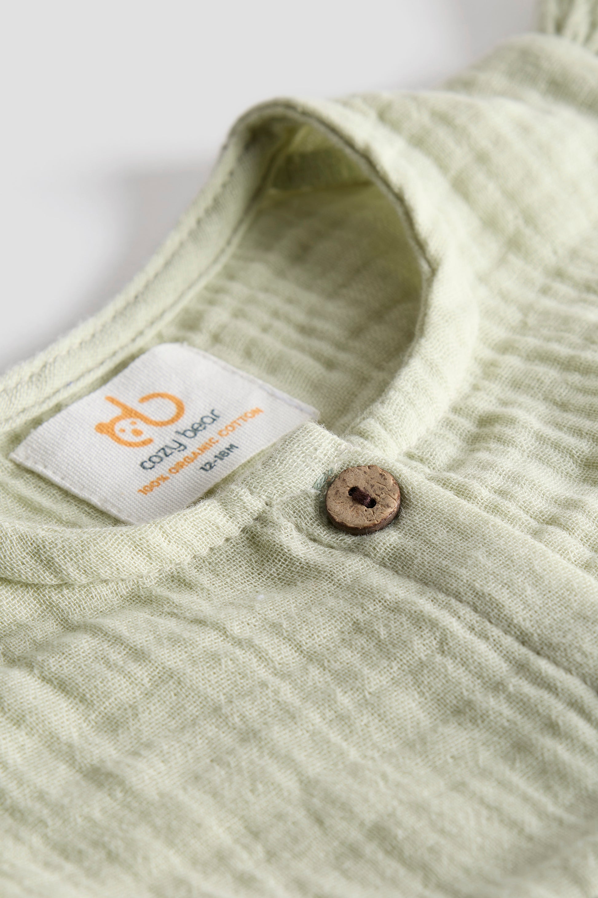 Close-up of a light green fabric with a button and a visible label on a white background