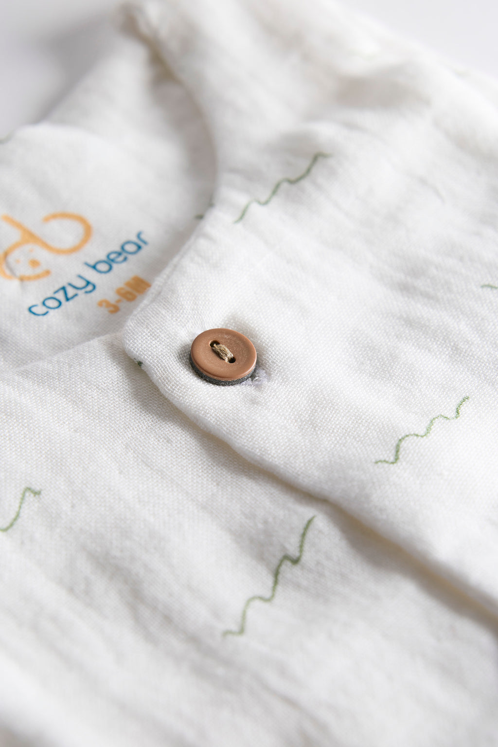 Close-up of a button on a white garment with 'cozy bear' branding.