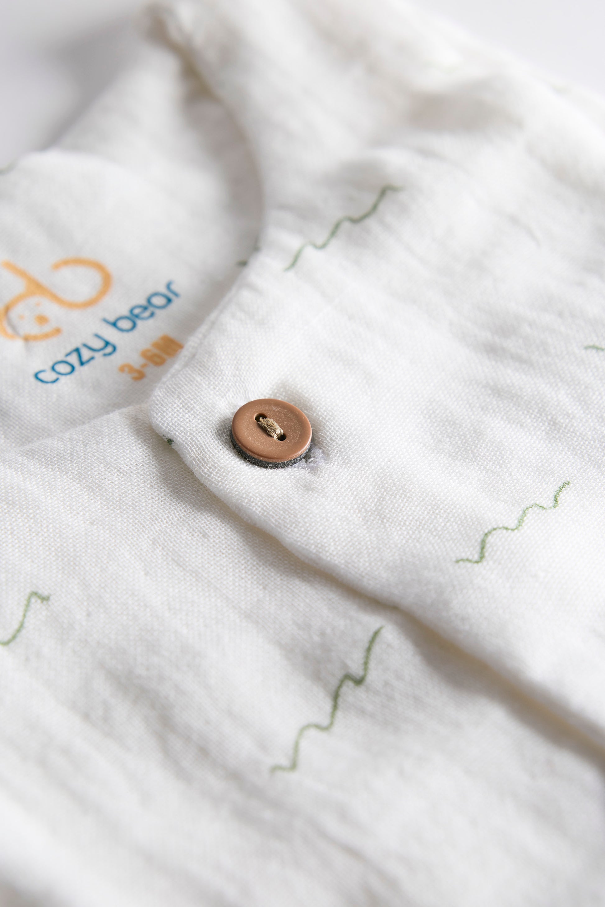 Close-up of a button on a white garment with 'cozy bear' branding.
