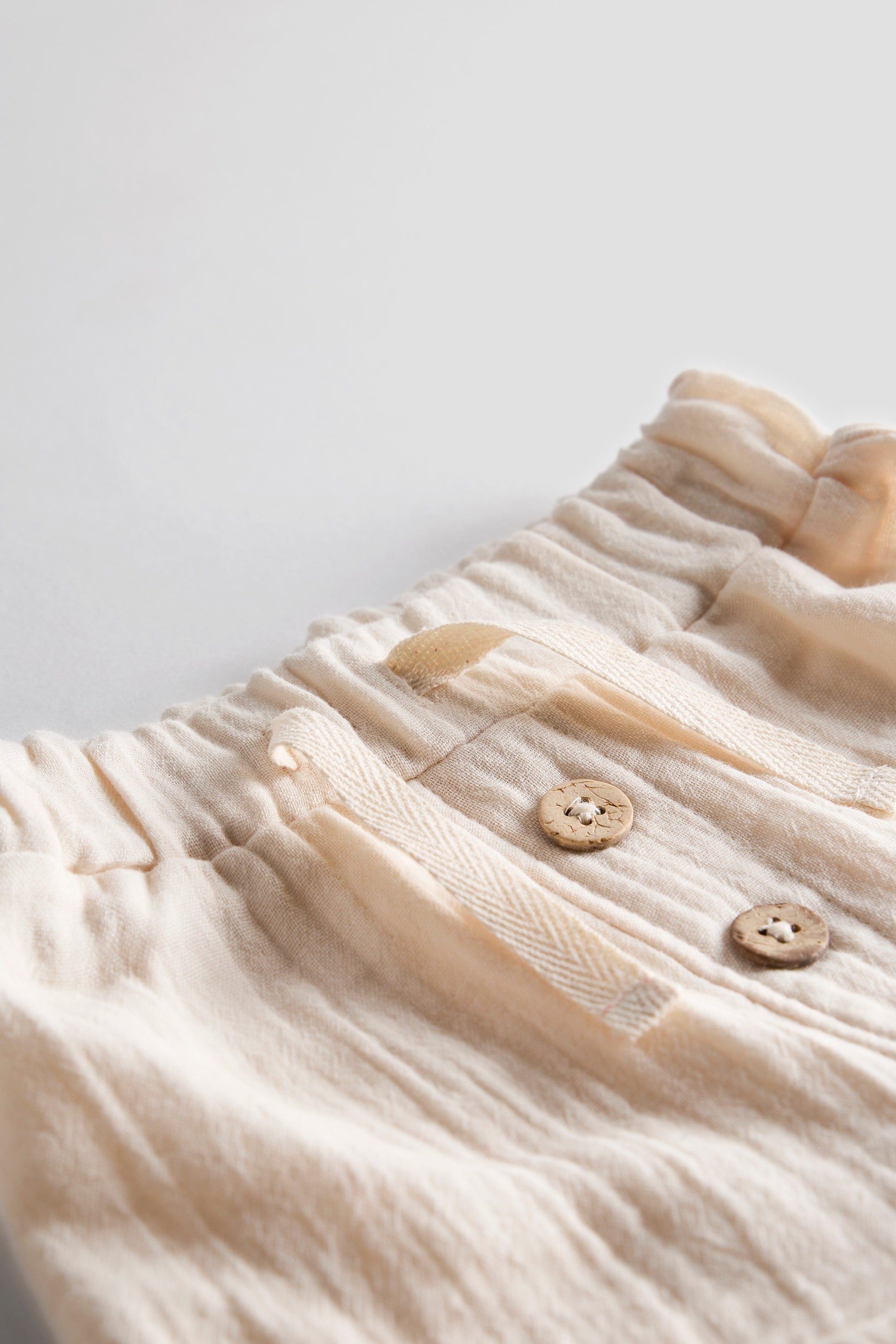 Close-up of a beige textured fabric with buttons on a light gray background