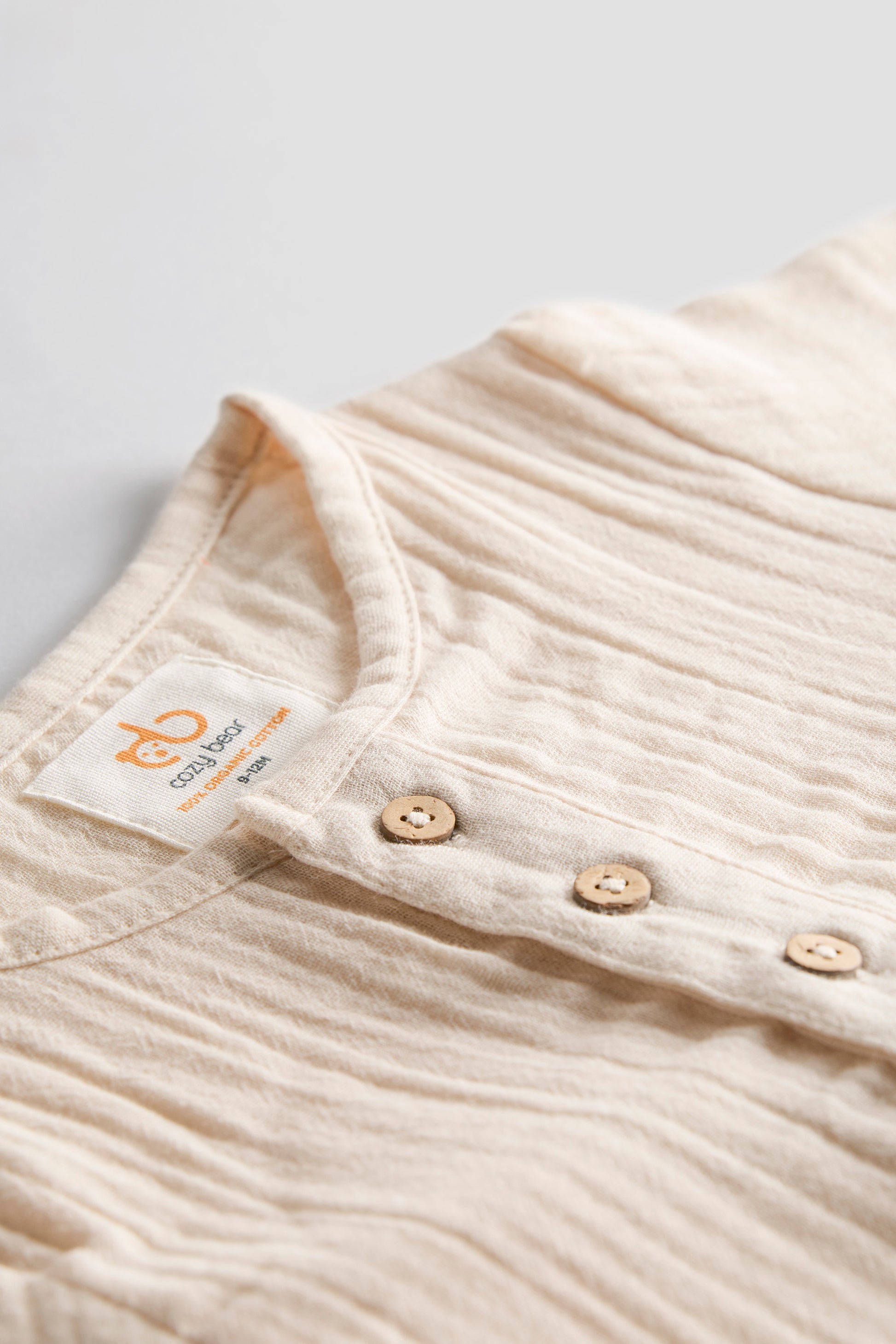 Close-up of a ribbed baby shirt with buttons and a visible label on a light background