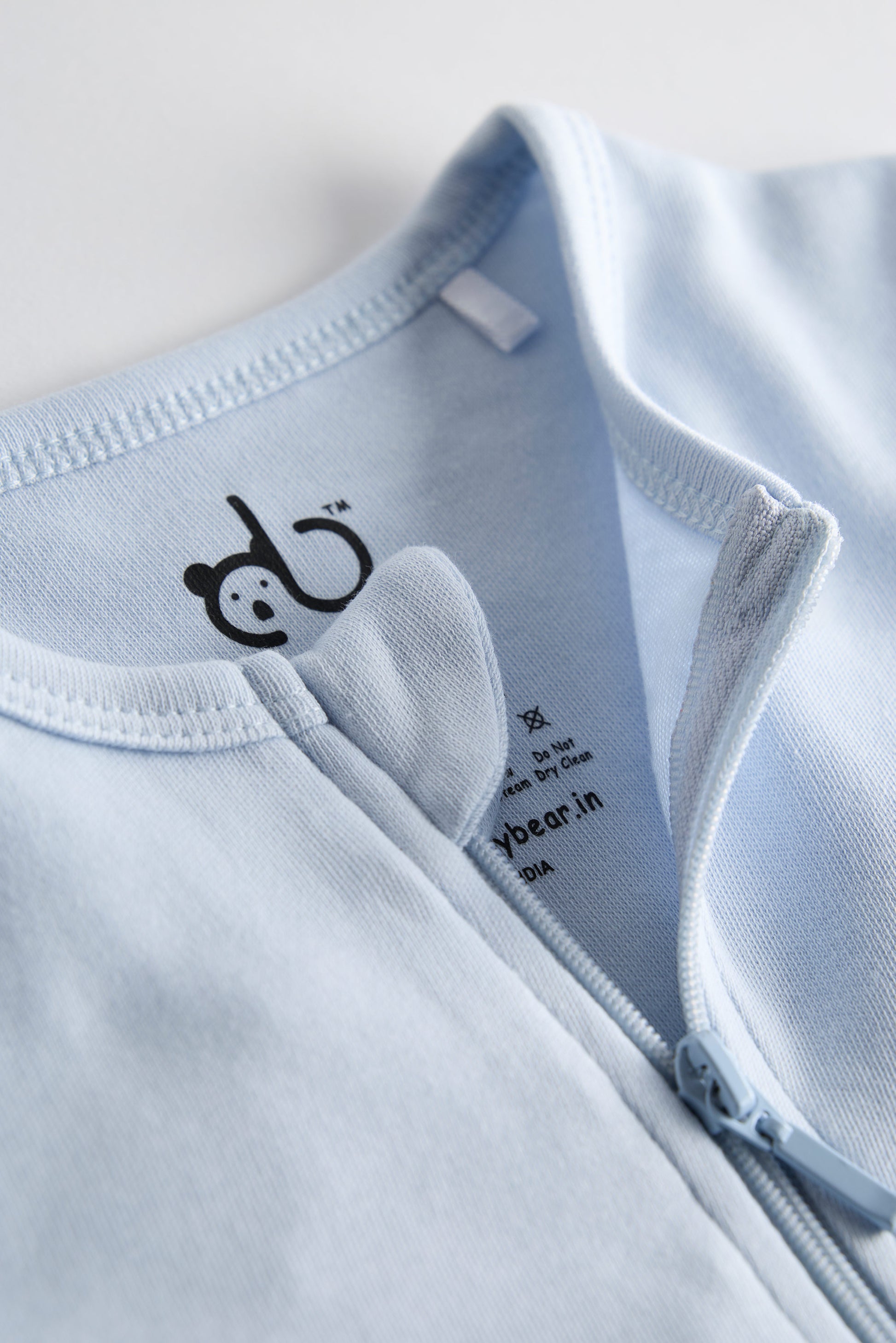 Close-up of a light blue baby outfit with a logo on a white background